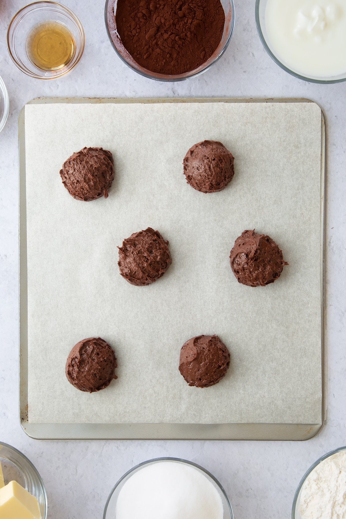 6 small balls of chocolate whoopie batter on a parchment lined baking tray.