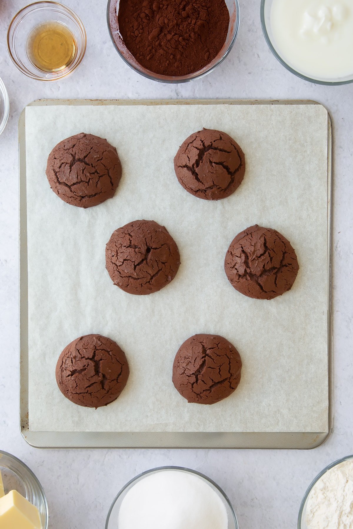 6 baked  chocolate whoopie cookies on a parchment lined baking tray.