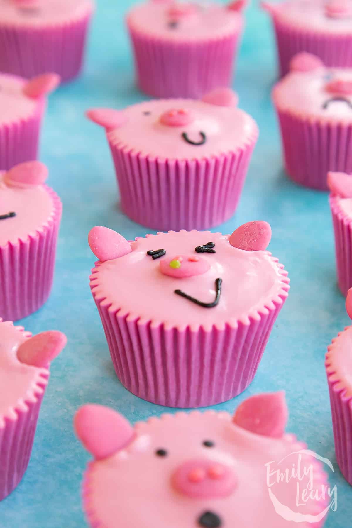 side view of pink pig cupcakes in pink cupcakes liners on a blue background.