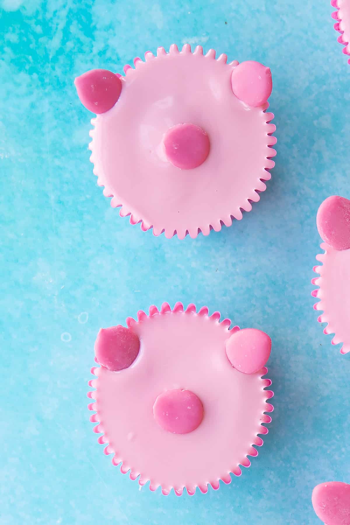 pink chocolate topping on a pink cupcake in a pink cupcake liner with 3 dark pink chocolate drops to create ears and a nose.