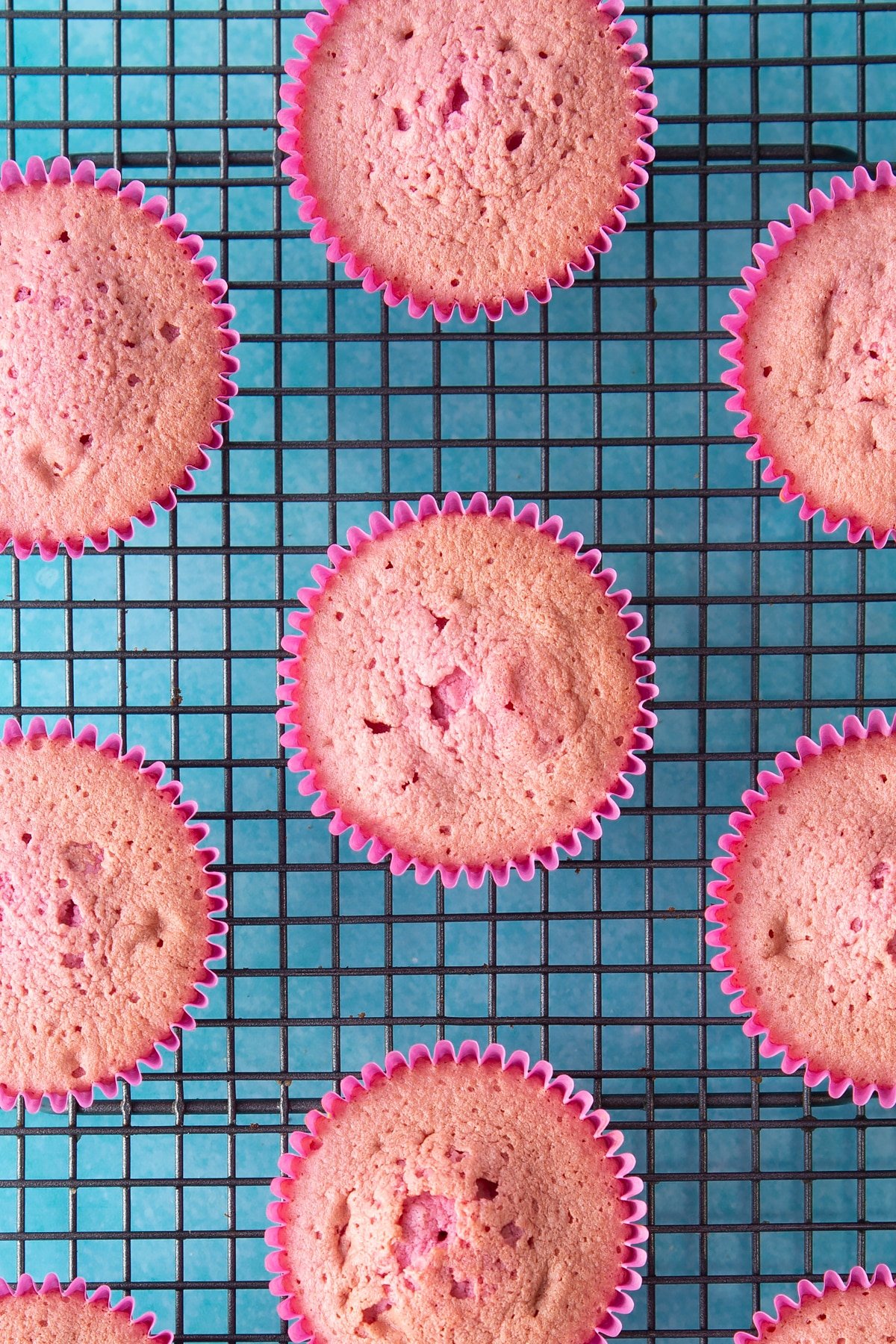 baked pink cupcakes in pink cupcake liners ona wire cooling tray.