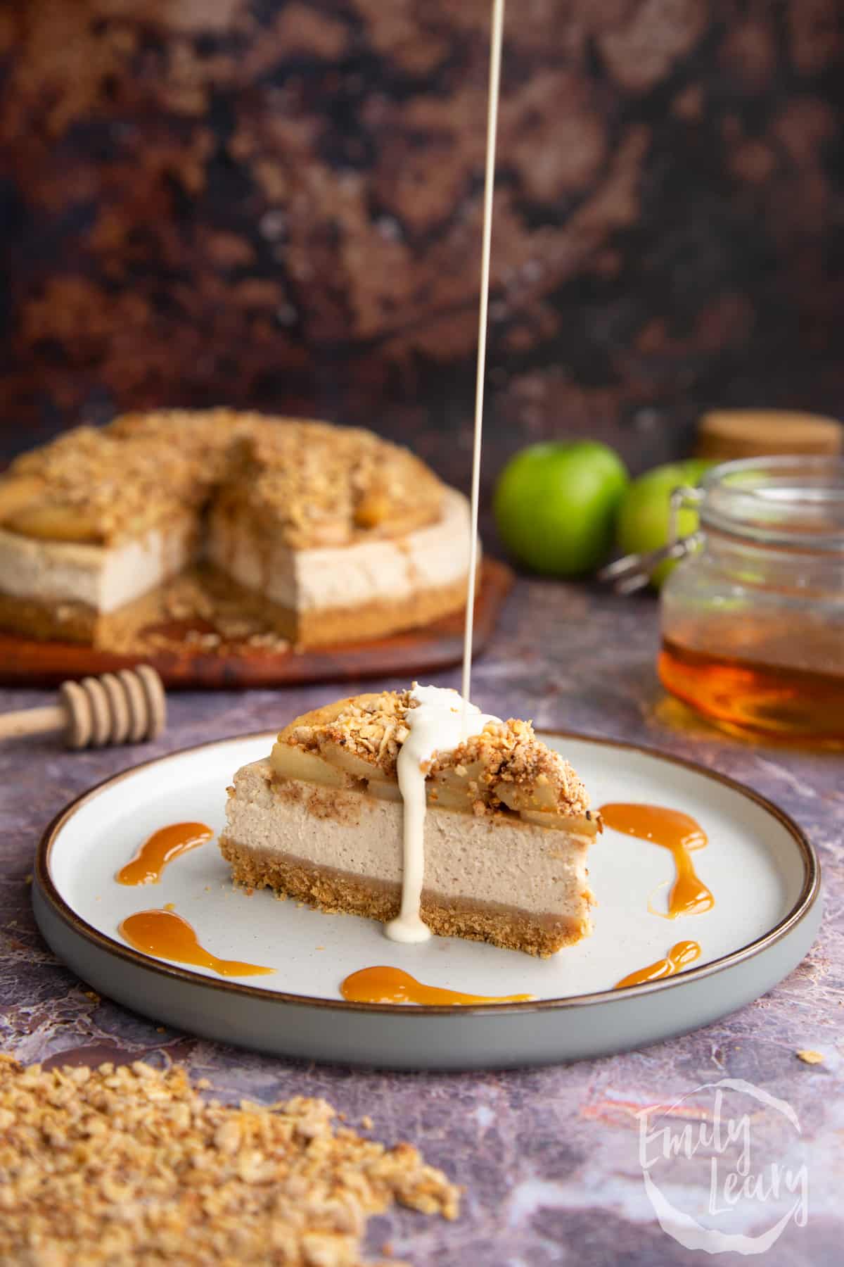 Adding a drizzle of cream onto a slice of the finished apple crumble cheesecake.