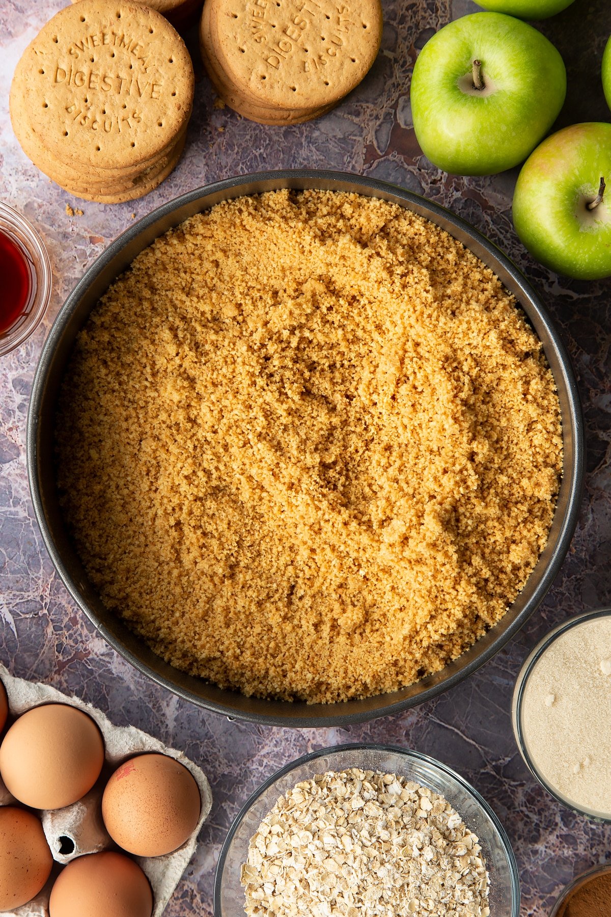 Adding the biscuit crumb base into a large round baking tin. 