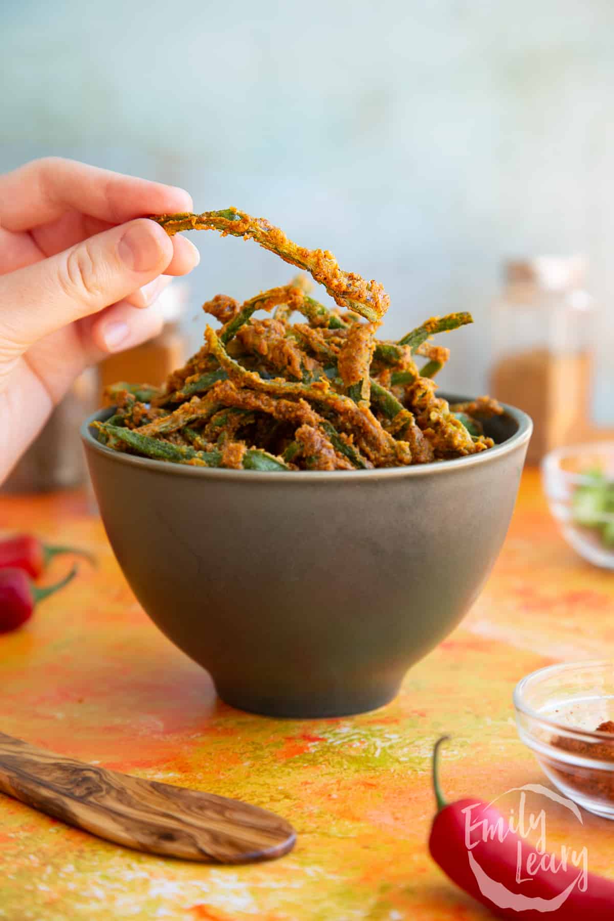 Side on shot of a hand reaching in to grab a finished piece of kurkuri bhindi. 