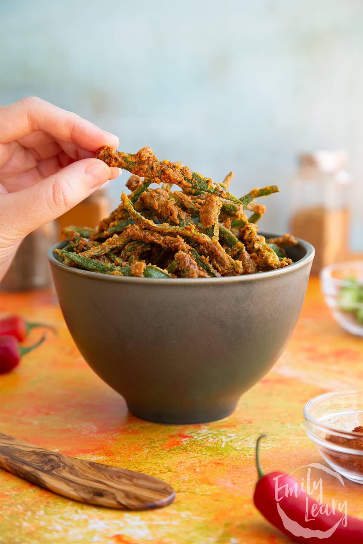 Hand reaching in to grab a finished piece of kurkuri bhindi out of the dark bowl.