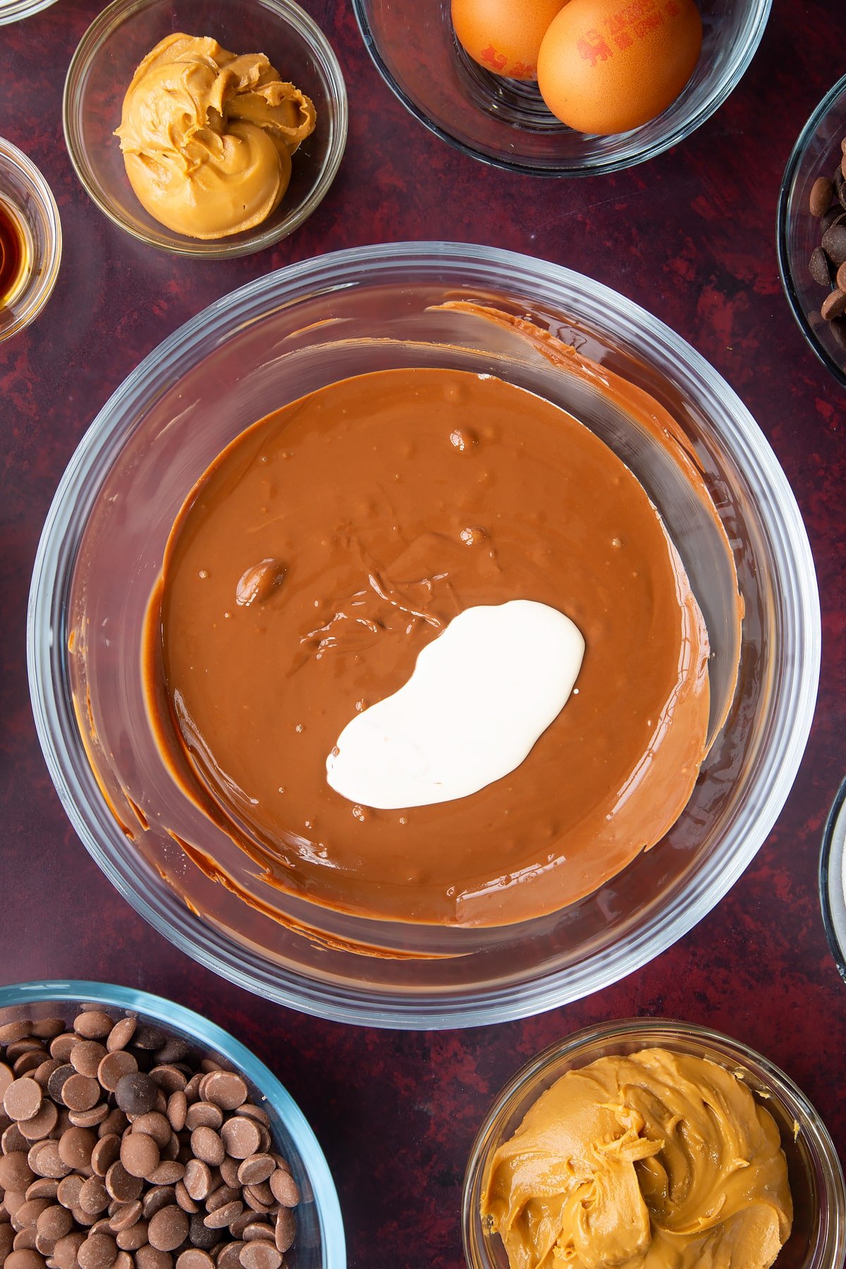 melted chocolate and peanut butter mix topped with cream in a large clear bowl.
