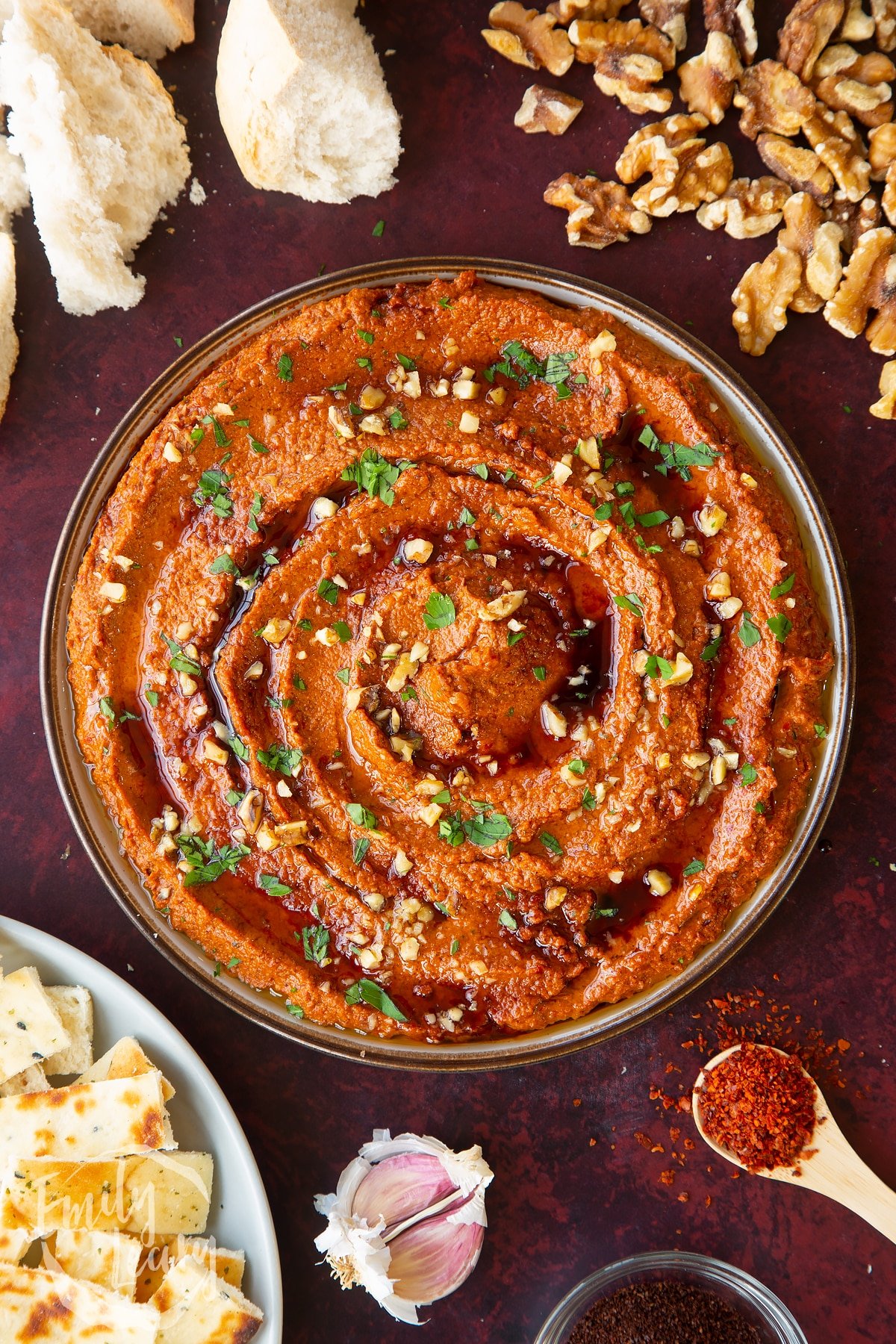 overhead shot of red pepper dip topped with fresh herbs and toasted walnuts in a dish.