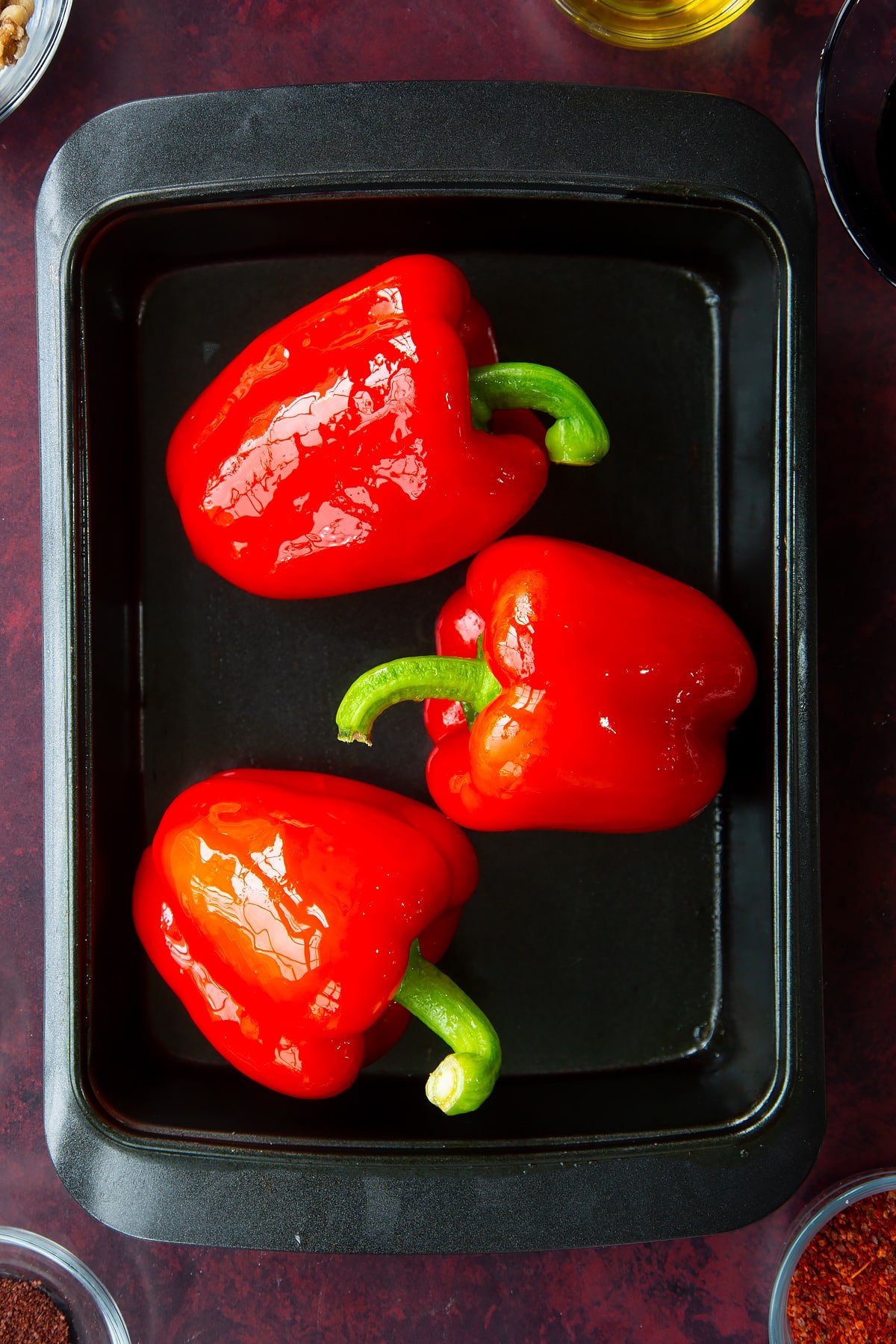 3 whole red peppers in a roasting dish.