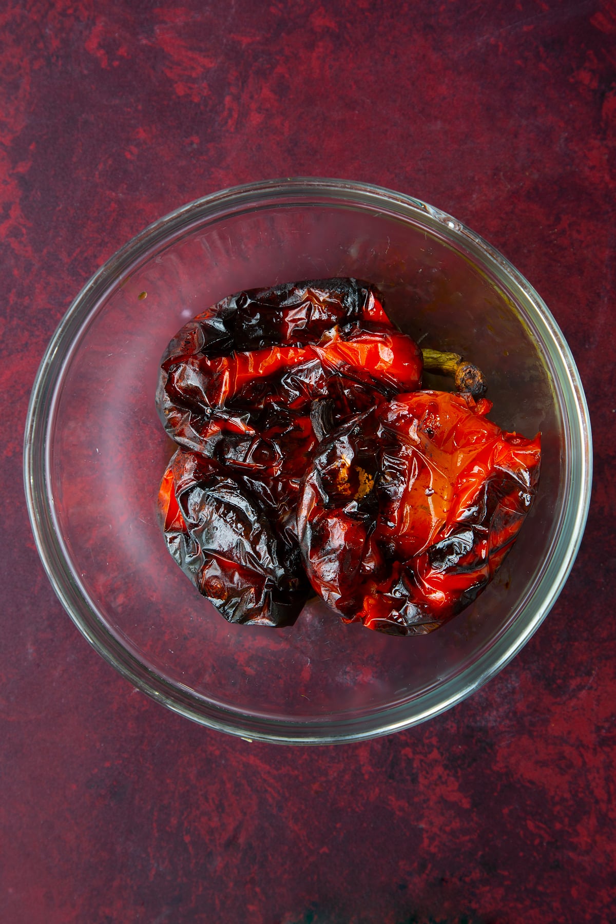 3 whole roasted  red peppers in a clear dish.