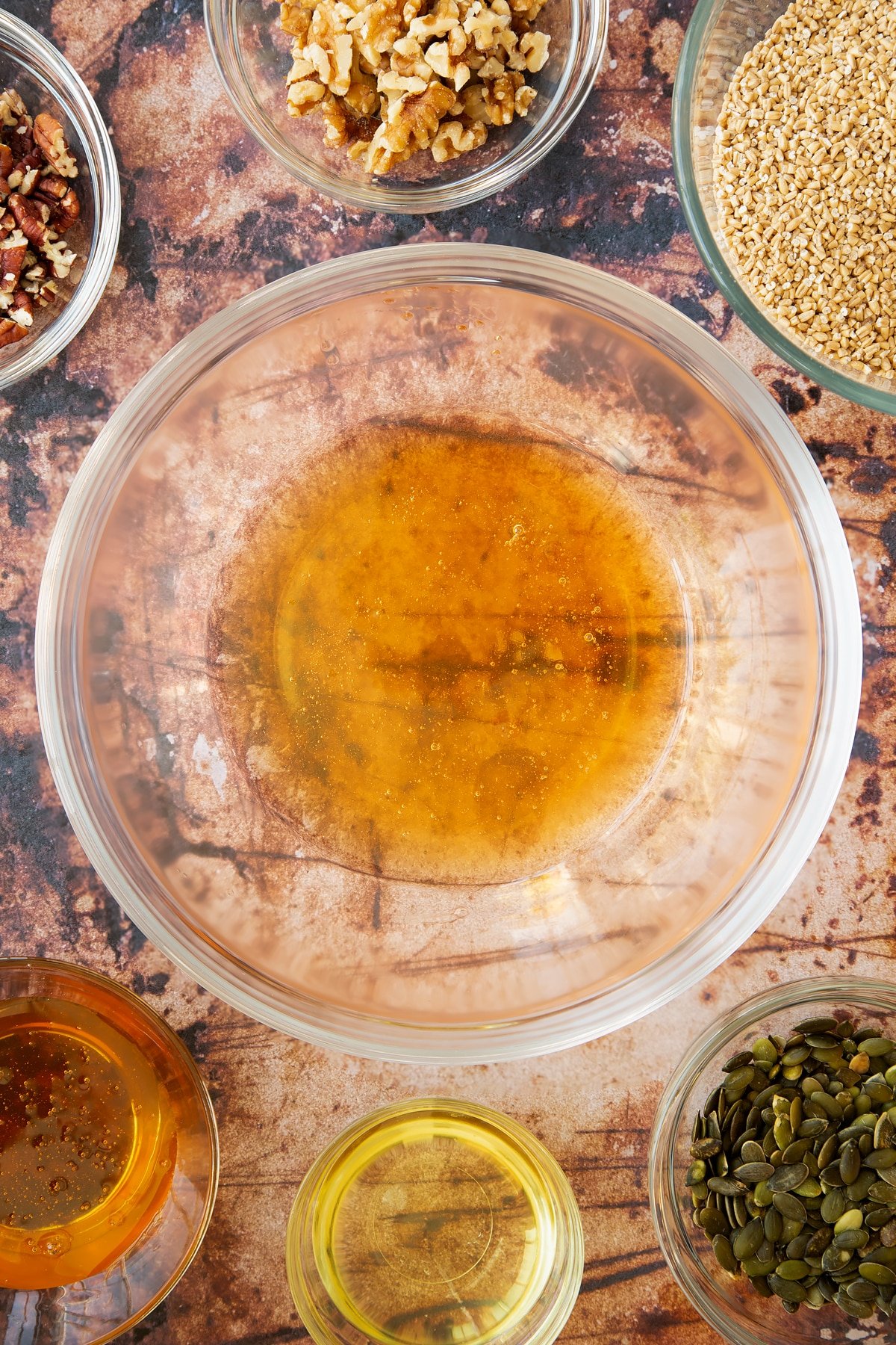 oil and honey in a large clear bowl. surrounded by ingredients.