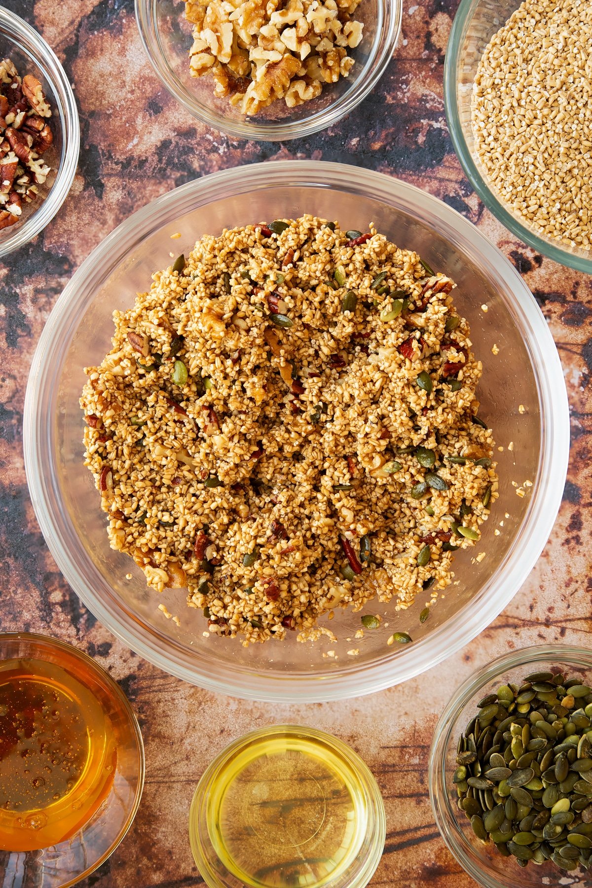 steel cut oats, pumpkin seeds, pecans and walnuts coated in honey and oil in a large clear bowl