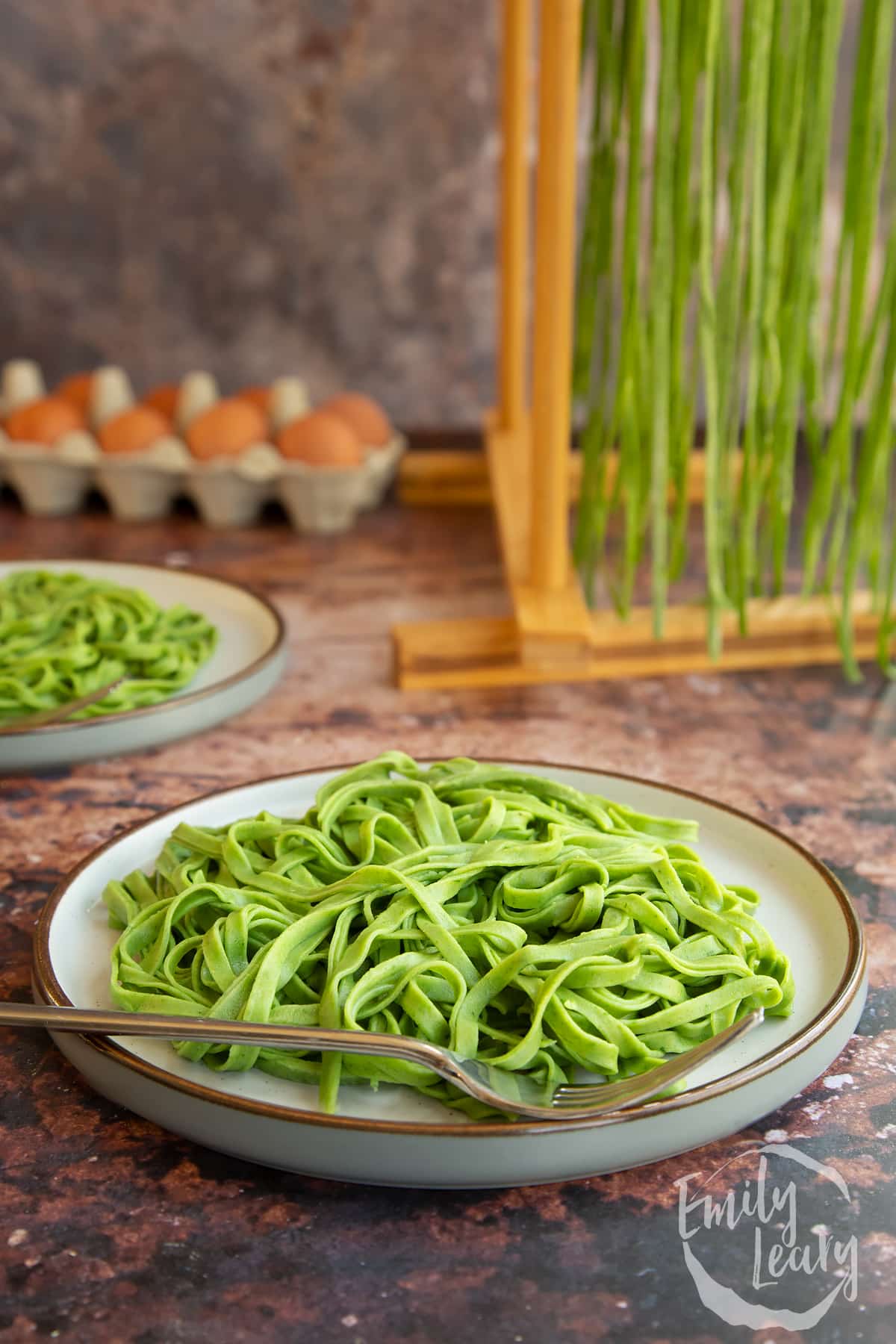 Tagliatelle verdi on a white plate with a fork at the front with another plate in the background.