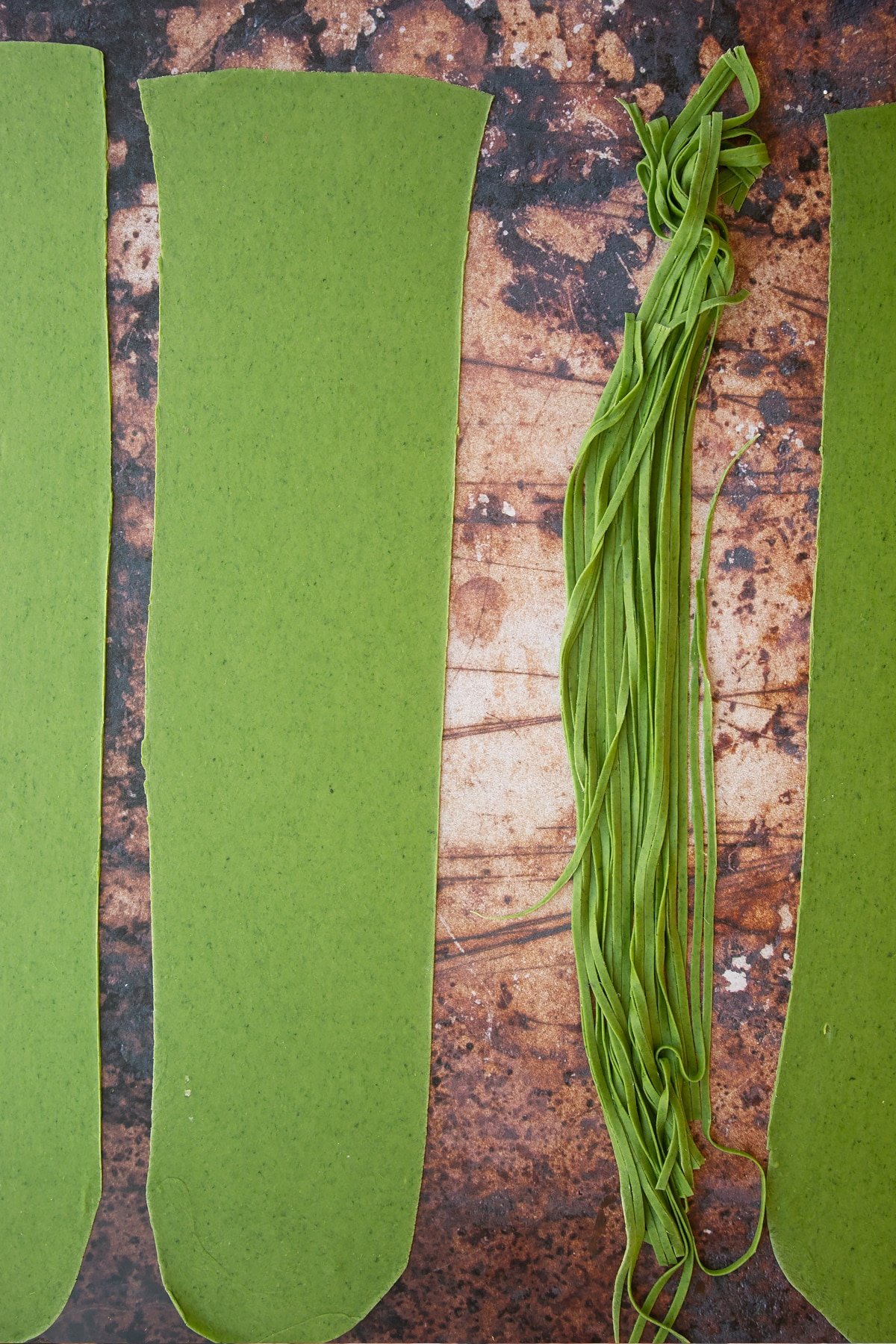 tagliatelle verdi pasta cut into thin strips on a brown background.