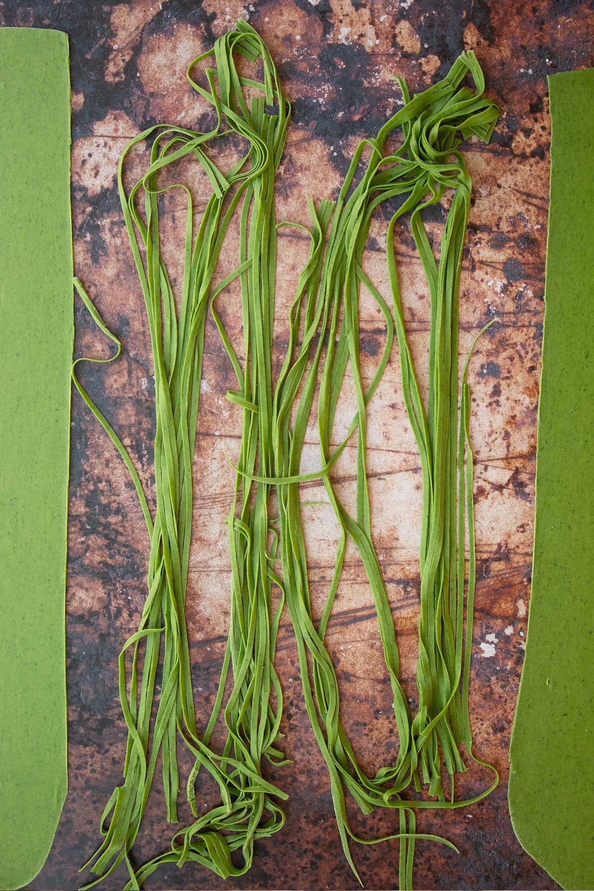 tagliatelle verdi pasta cut into thin strips on a brown background.