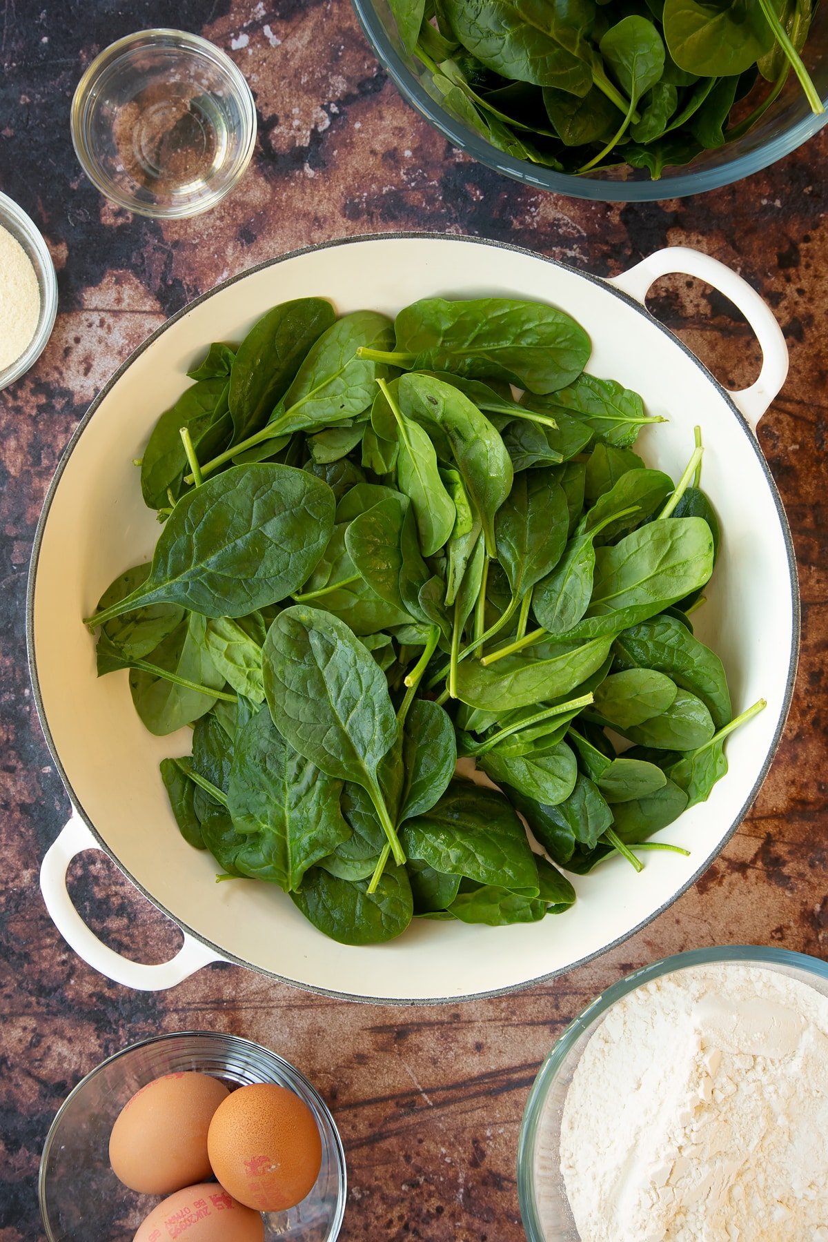 a large white pan filled with uncooked spinach.
