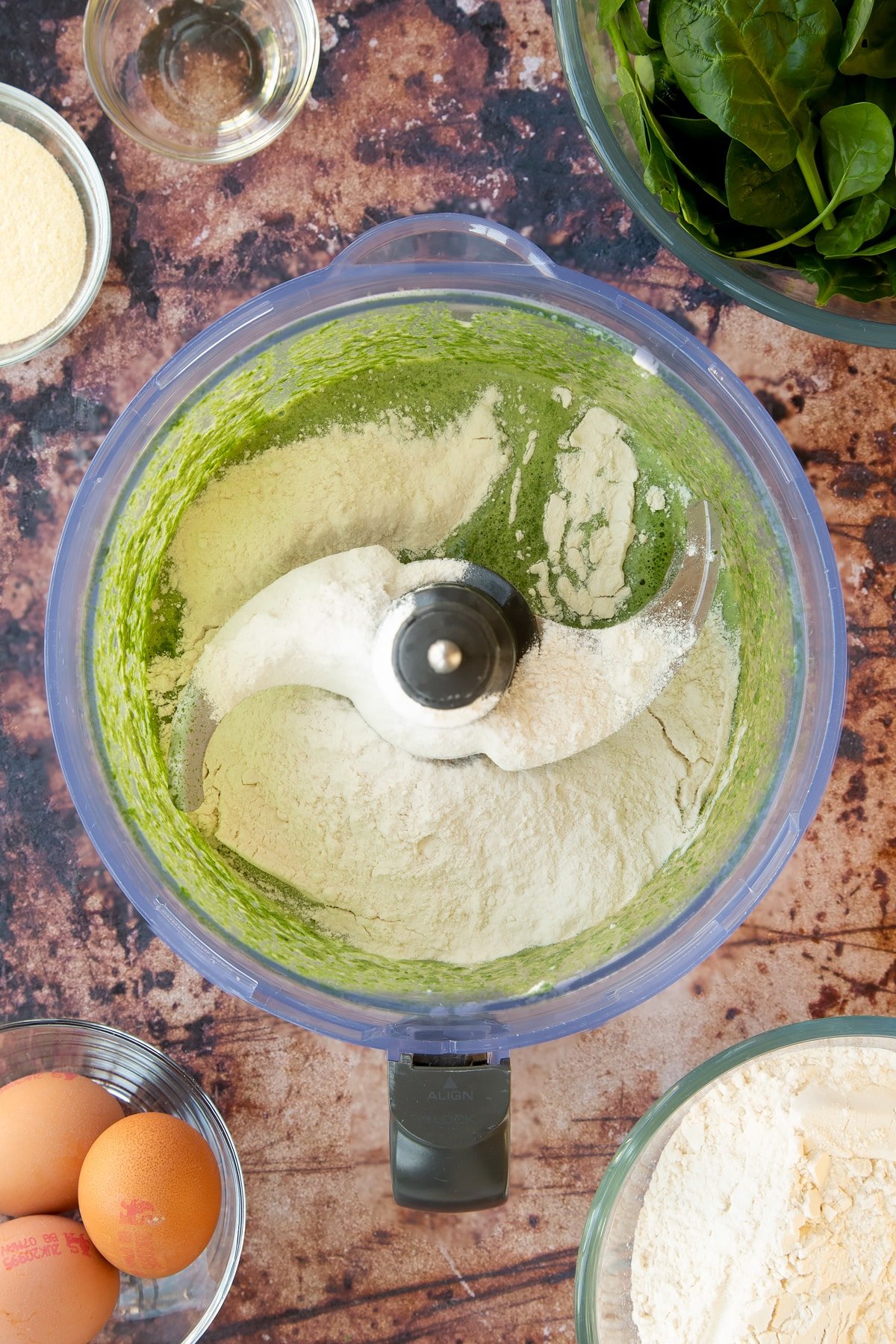 green spinach and egg mixture topped with flour in a food processor.
