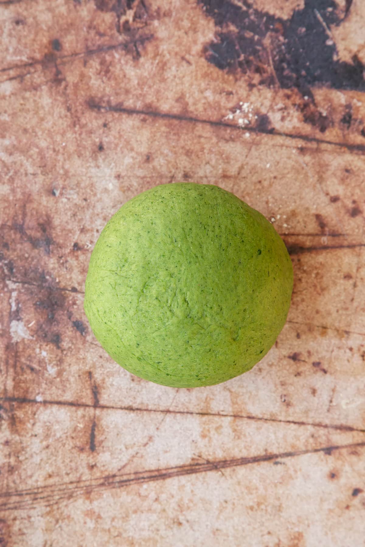 kneaded green pasta dough on a brown background.