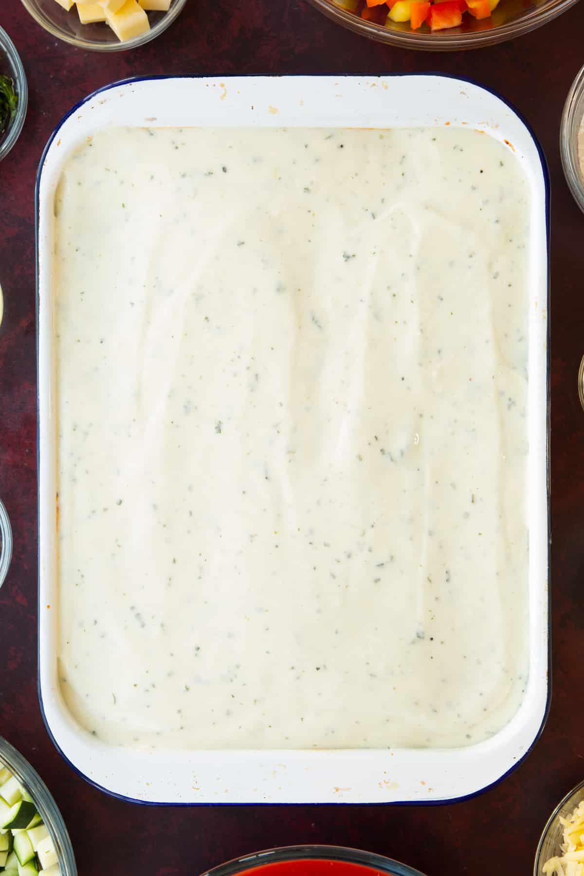 Overhead shot of the white / cheese sauce layered ontop of the potatoes in a tray.