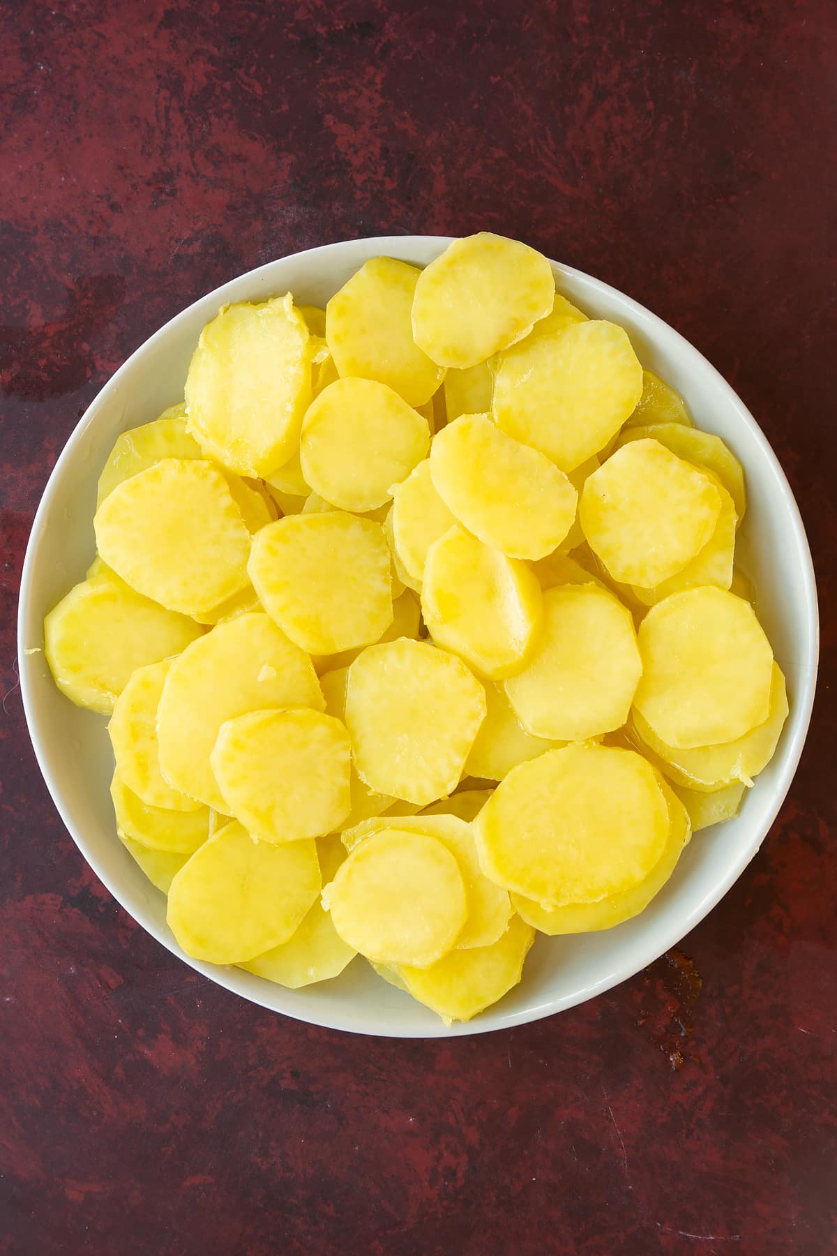 Overhead shot of the sliced potatoes in a white bowl.