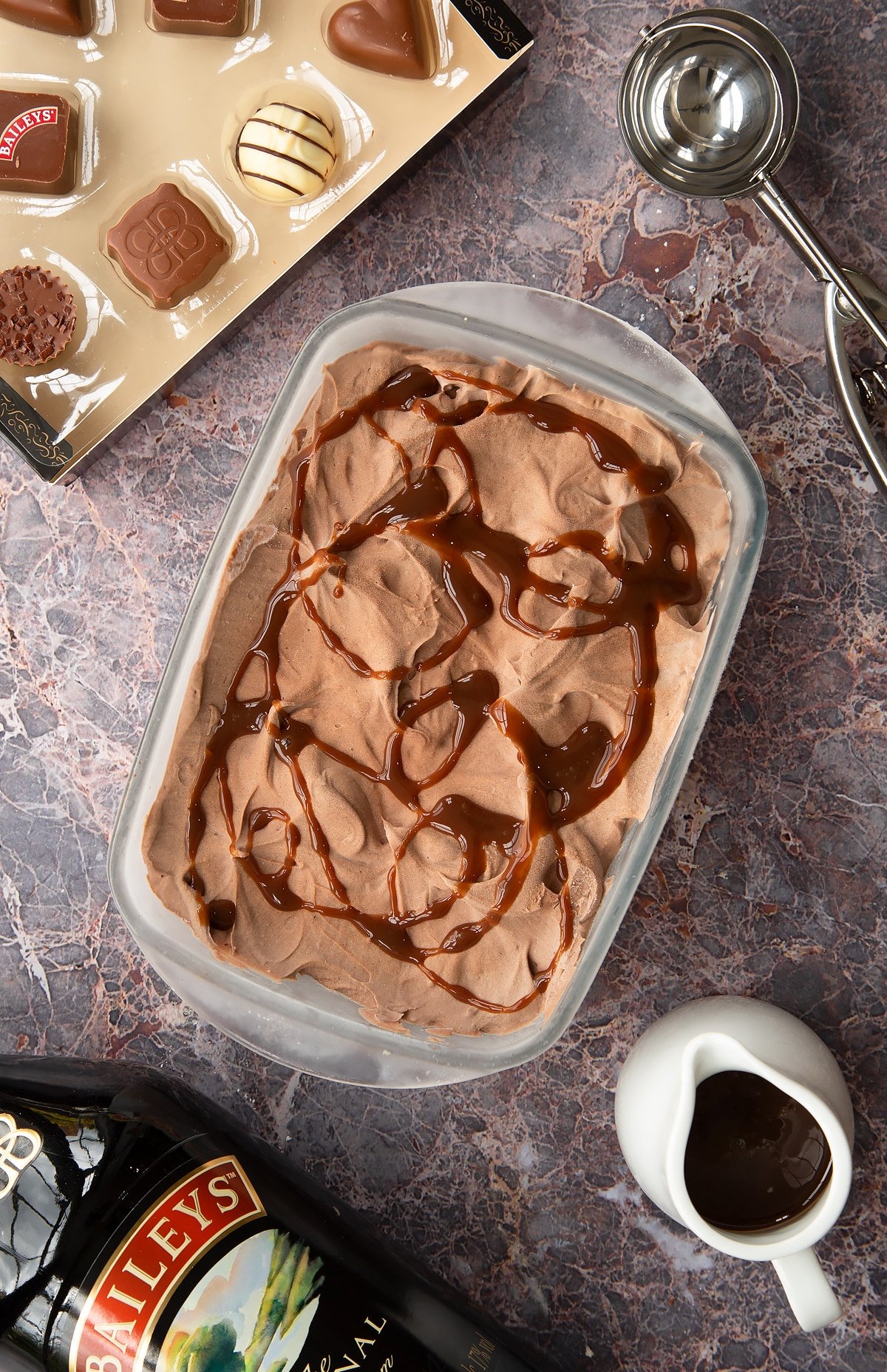 bailey ice cream mixture in a frozen pyrex dish topped with chocolate sauce with baileys chocolates at the side.