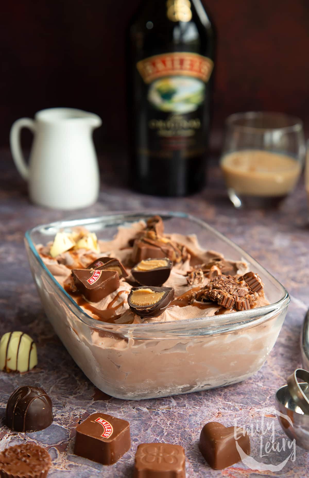 a side view of baileys ice cream in a pyrex dish topped with baileys chocolates on a marble background.