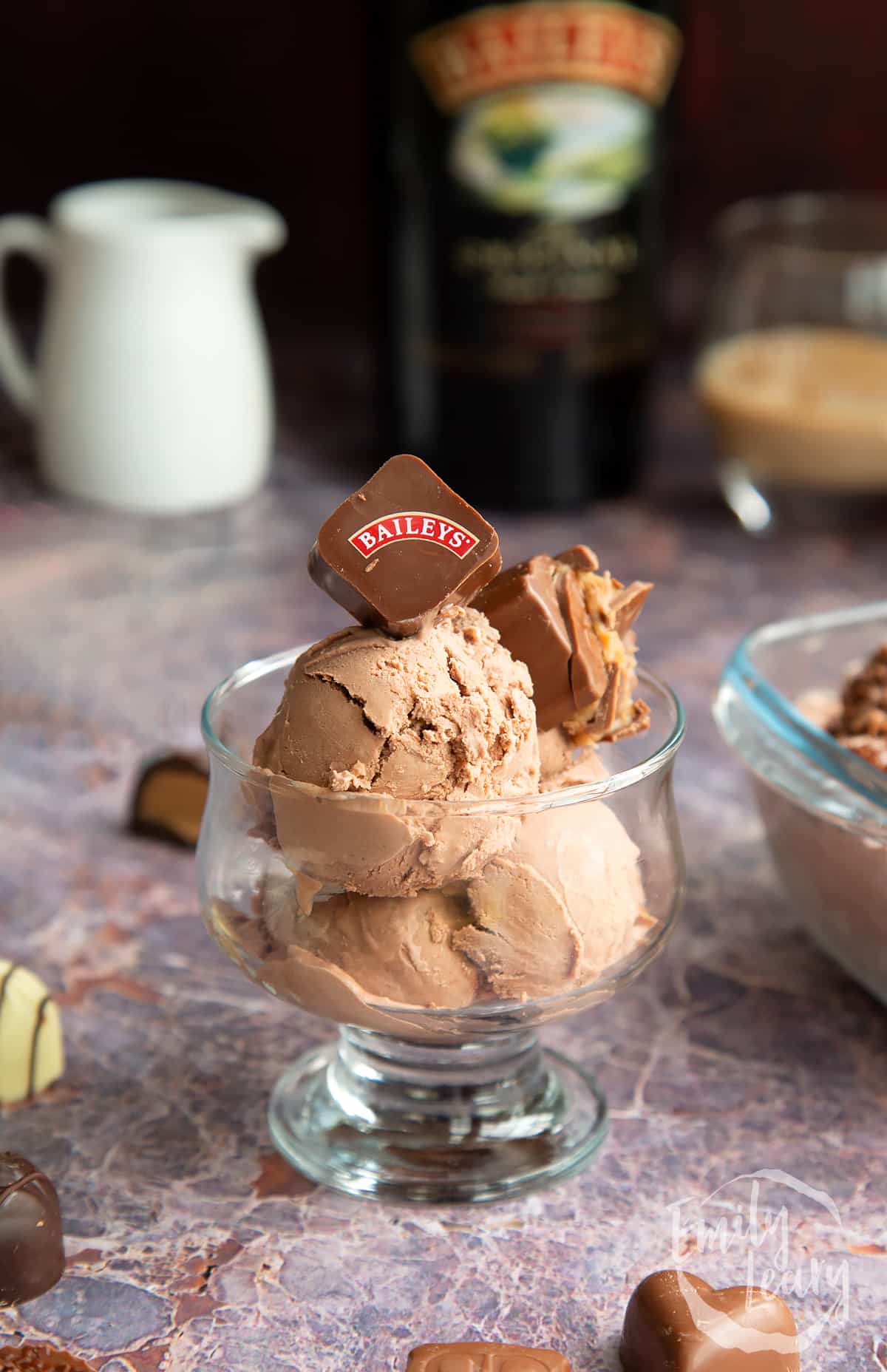 a side view of bailey ice cream in. a glass dessert dish topped with a baileys branded chocolate.