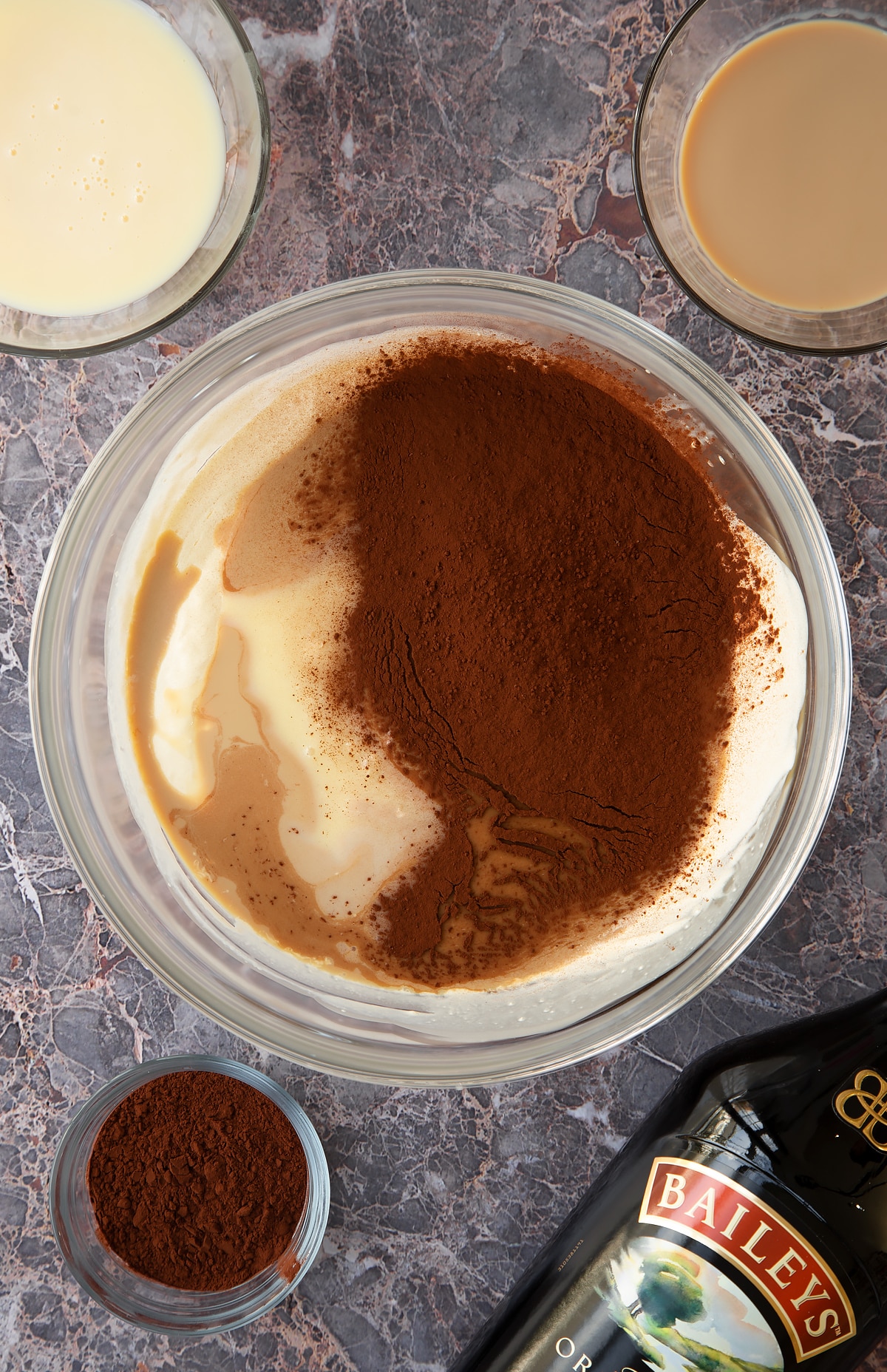 whisked cream topped with  condensed milk and Baileys and cococa powder in a large clear bowl.