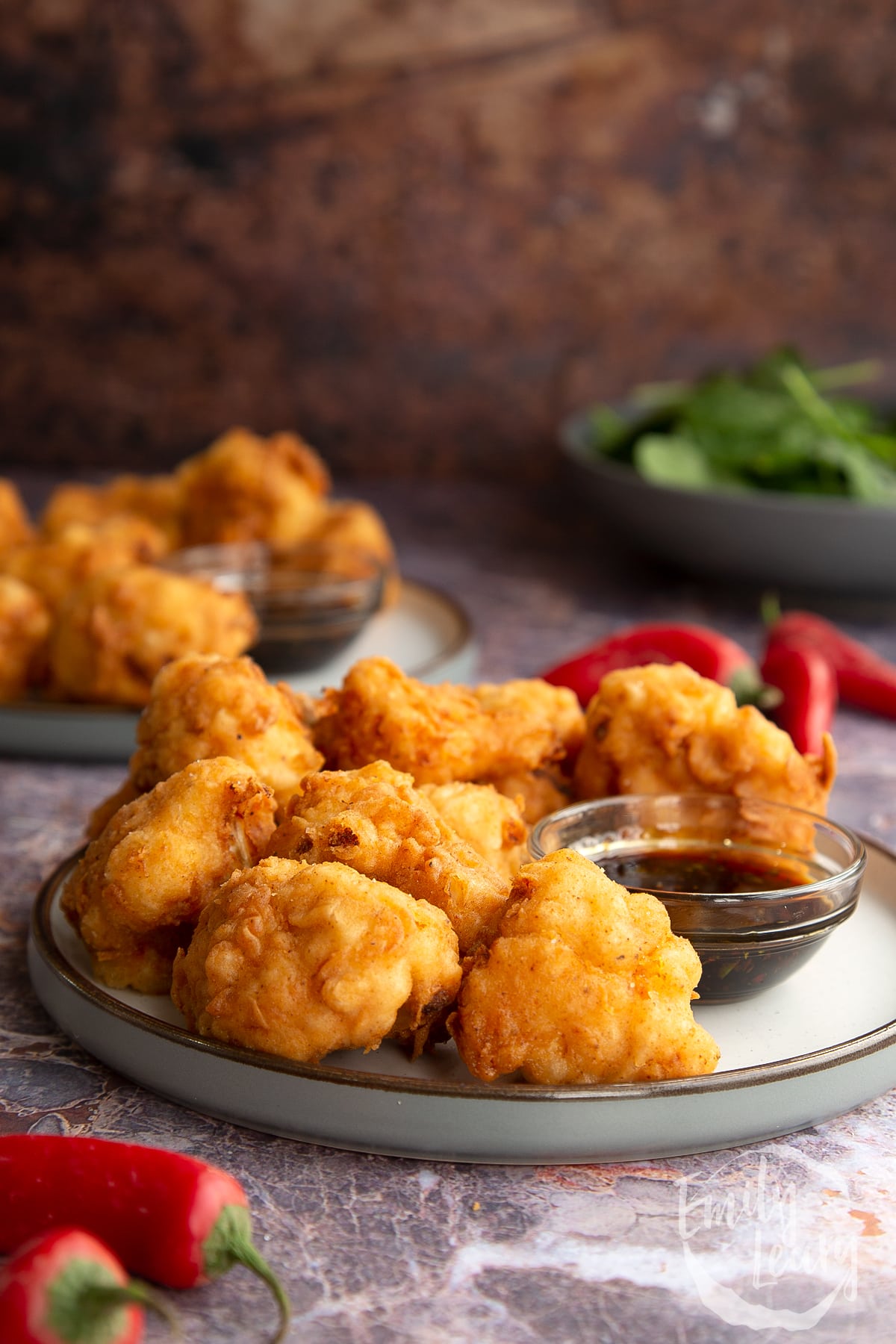 pieces of buttermilk fried cauliflower stacked on a grey plate with BBQ dipping sauce on the side.