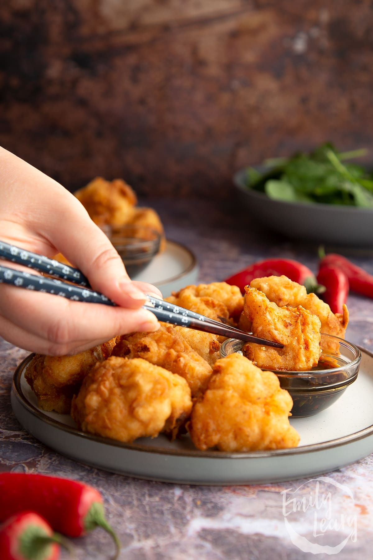 a hand holding chopsticks holding a piece of buttermilk fried chicken in dipping sauce.