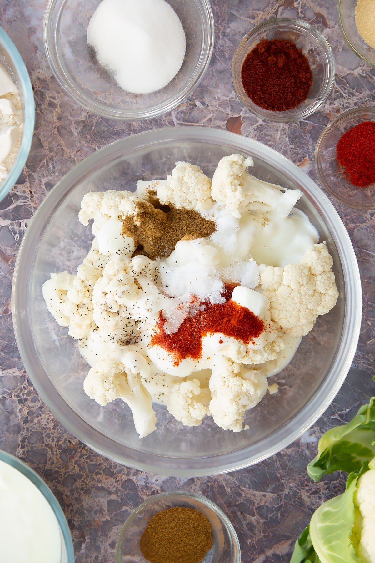 cauliflower florets topped with buttermilk, chilli powder, cumin and sugar in a clear bowl.