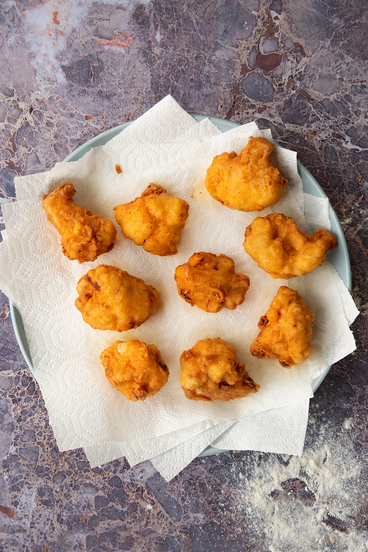 buttermilk fried cauliflower pieces on sheets of kitchen roll on a grey plate.