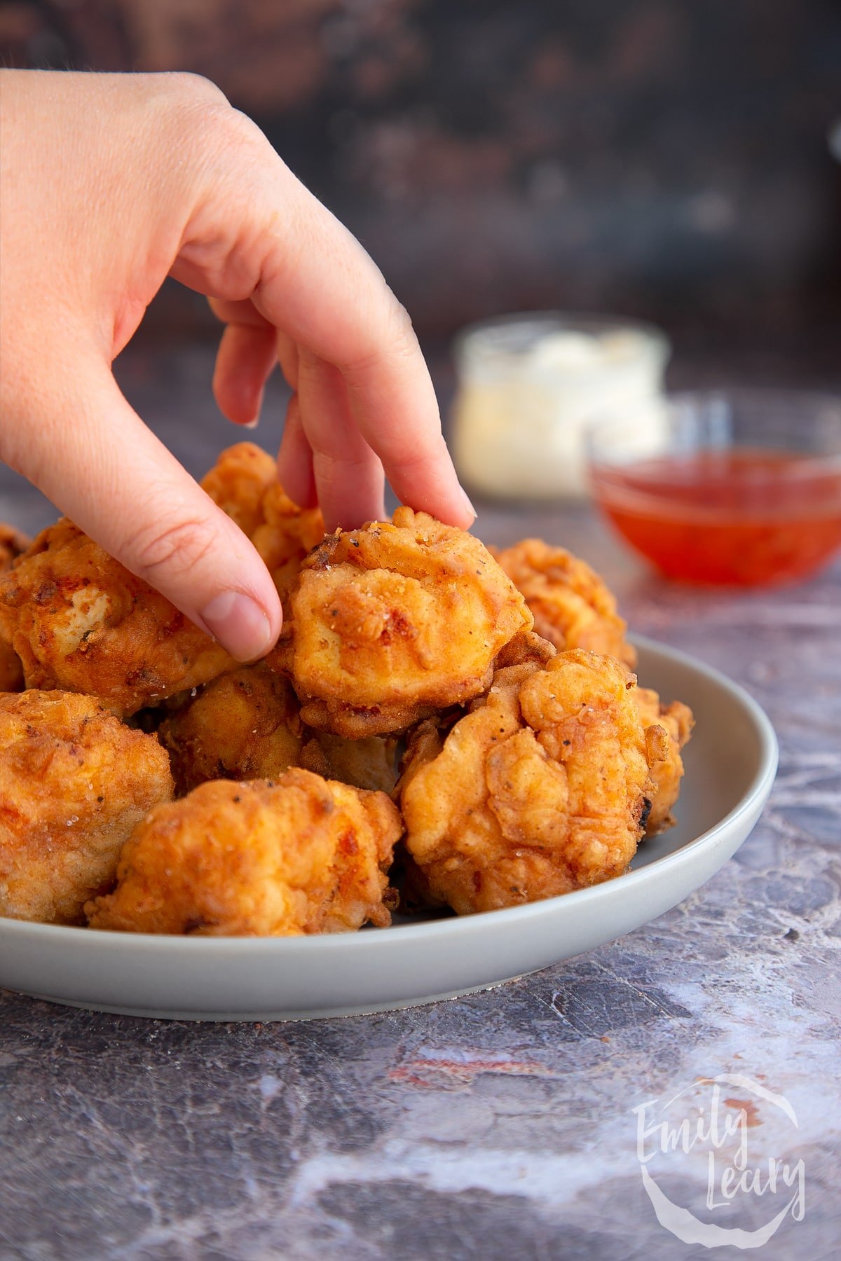 a hand picking up a piece of fried buttermilk tofu from a full white bowl.