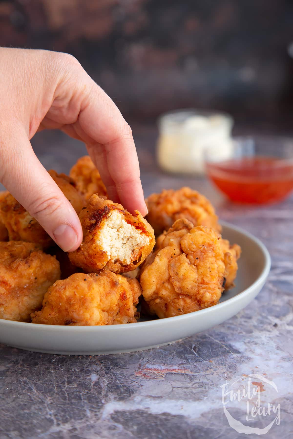 a hand holding a half bitten piece of Buttermilk fried tofu over a bowl of buttermilk fried tofu.