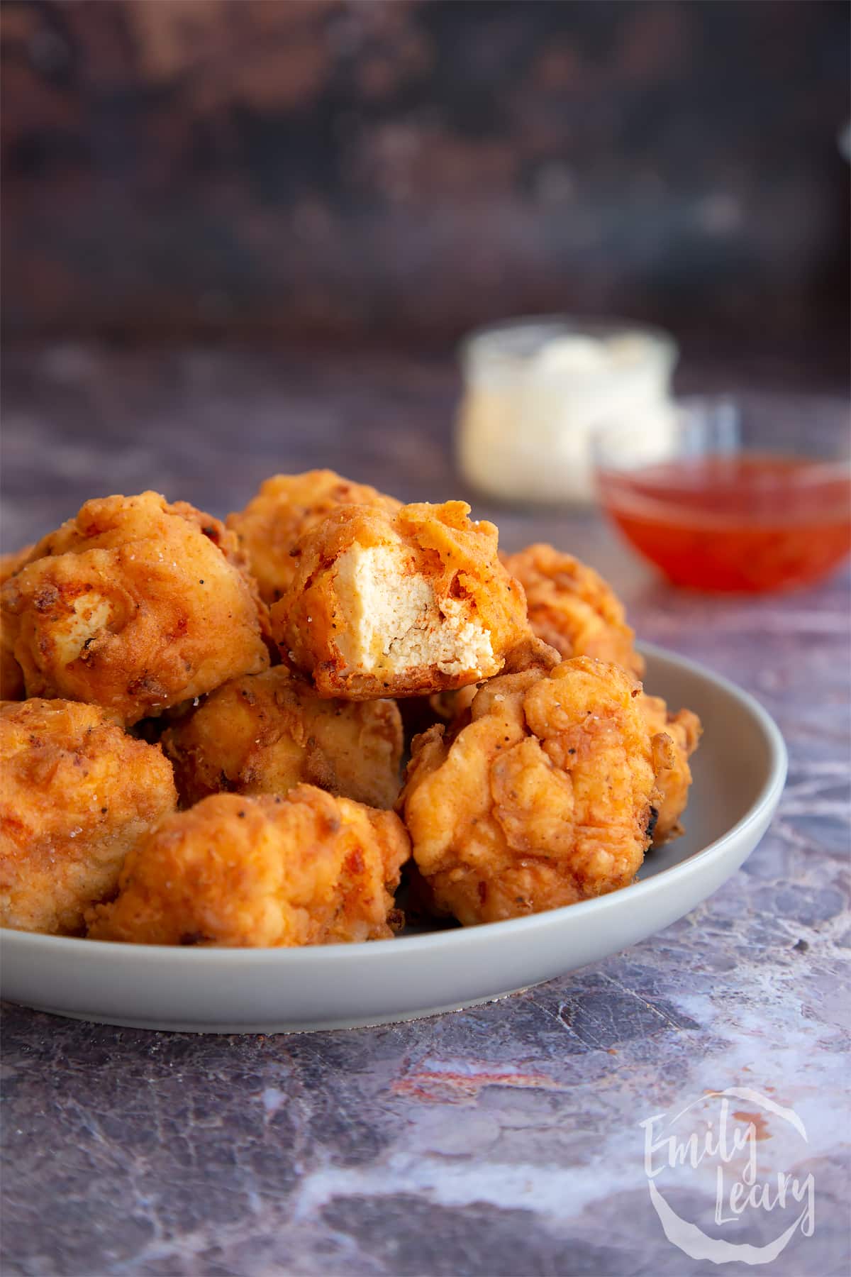 Buttermilk fried tofu stacked on a white plate with the top piece chopped in half.