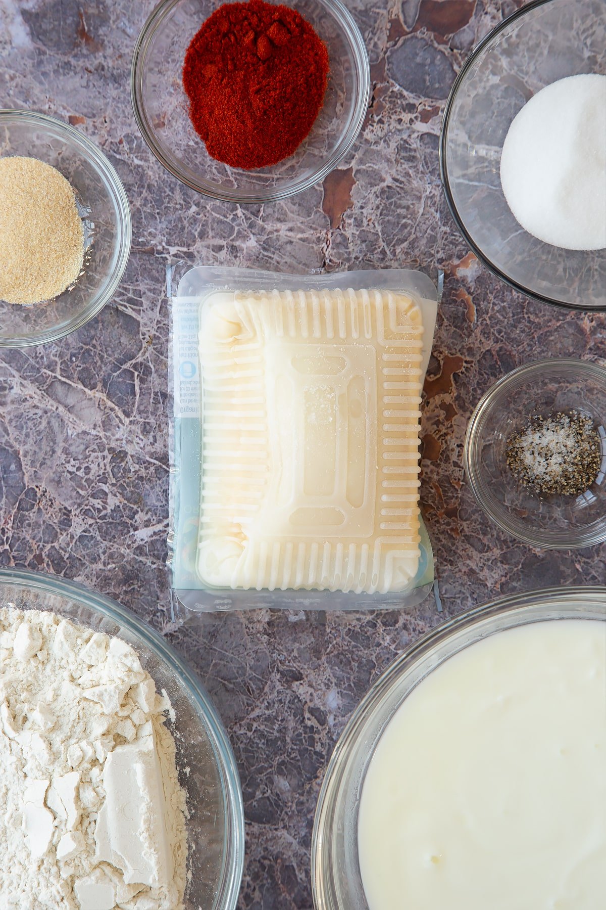 a frozen pack of tofu on a marble background saurrounded by spices and herbs.