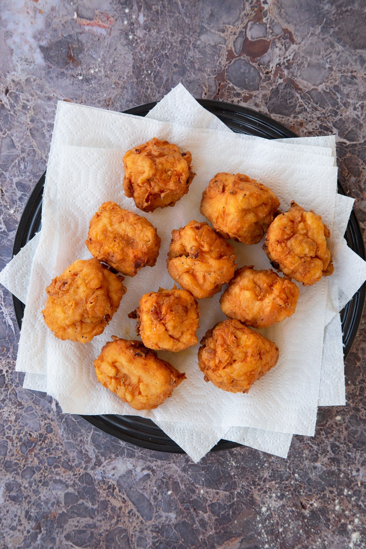 fried buttermilk tofu pieces on pieces of kitchen roll on a black plate.