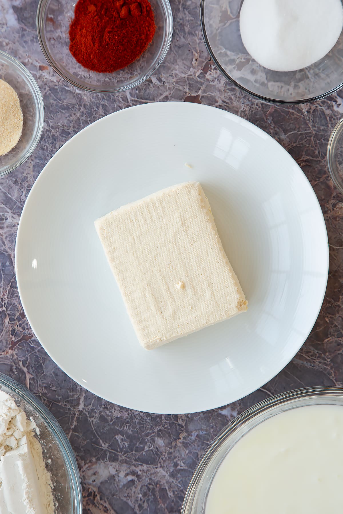 a block of tofu on a white plate surrounded by spices and herbs.