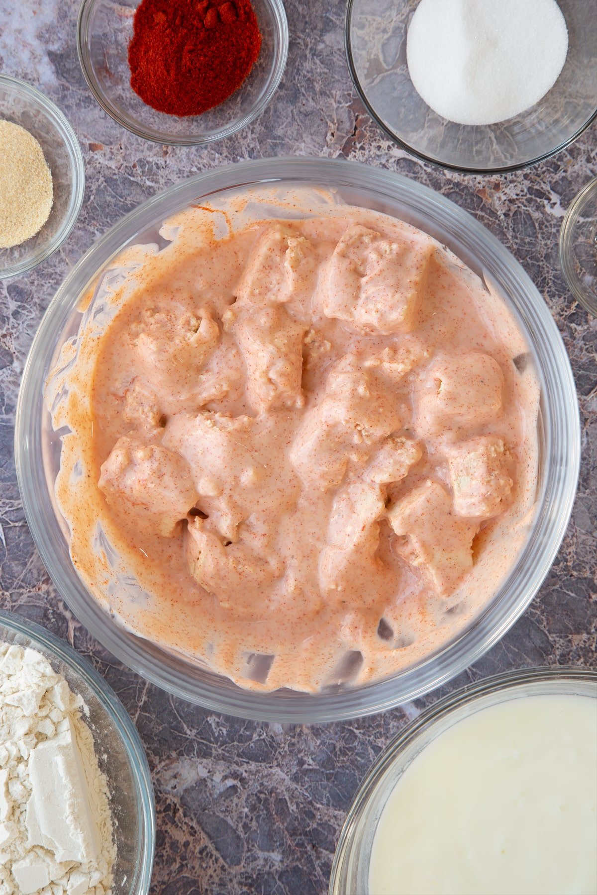 large crumb pieces of tofu covered in a paprika buttermilk marinade in a large clear bowl.