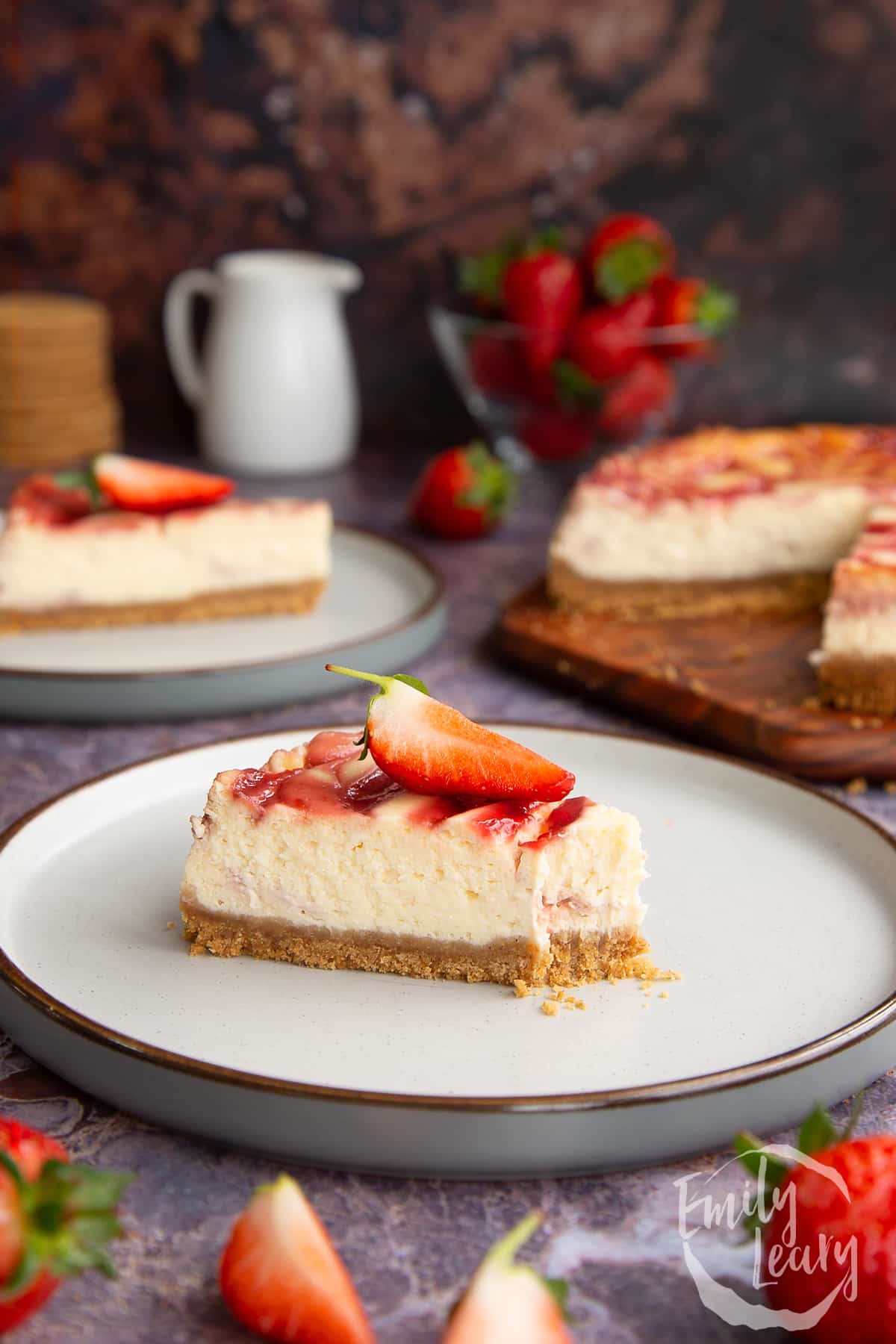 a slice of strawberry swirl cheesecake on a white plate topped with a chopped sttrawberry with a 
bite off the front.