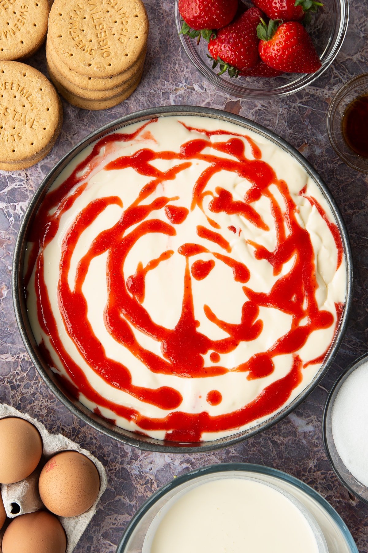 cheesecake batter in a springform cake tin topped with strawberry sauce.