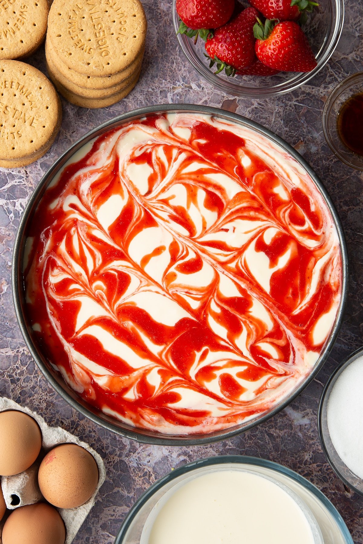 cheesecake batter in a springform cake tin topped with strawberry sauce in a swirled pattern.