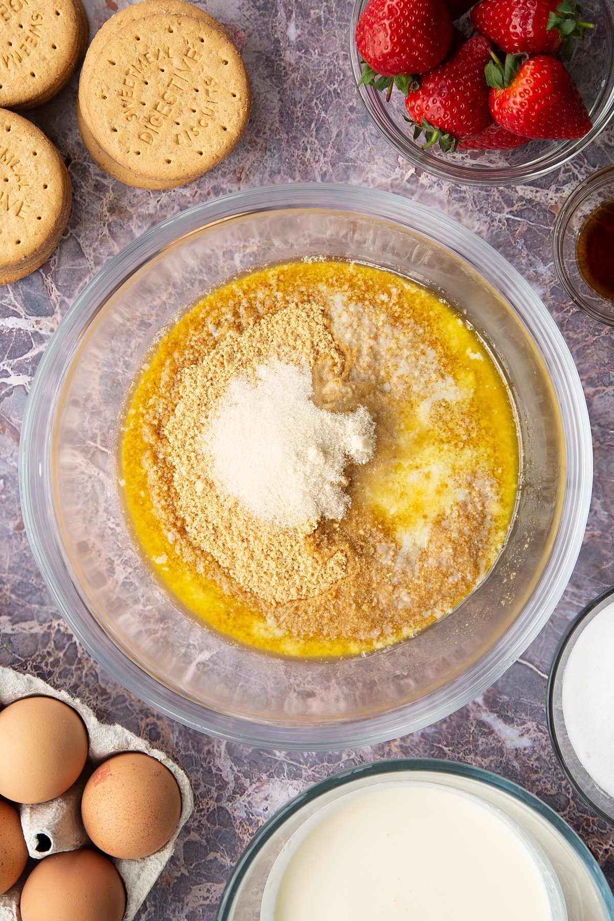 crushed digestive biscuit crumbs in a large clear bowl topped with white sugar and melted butter. 