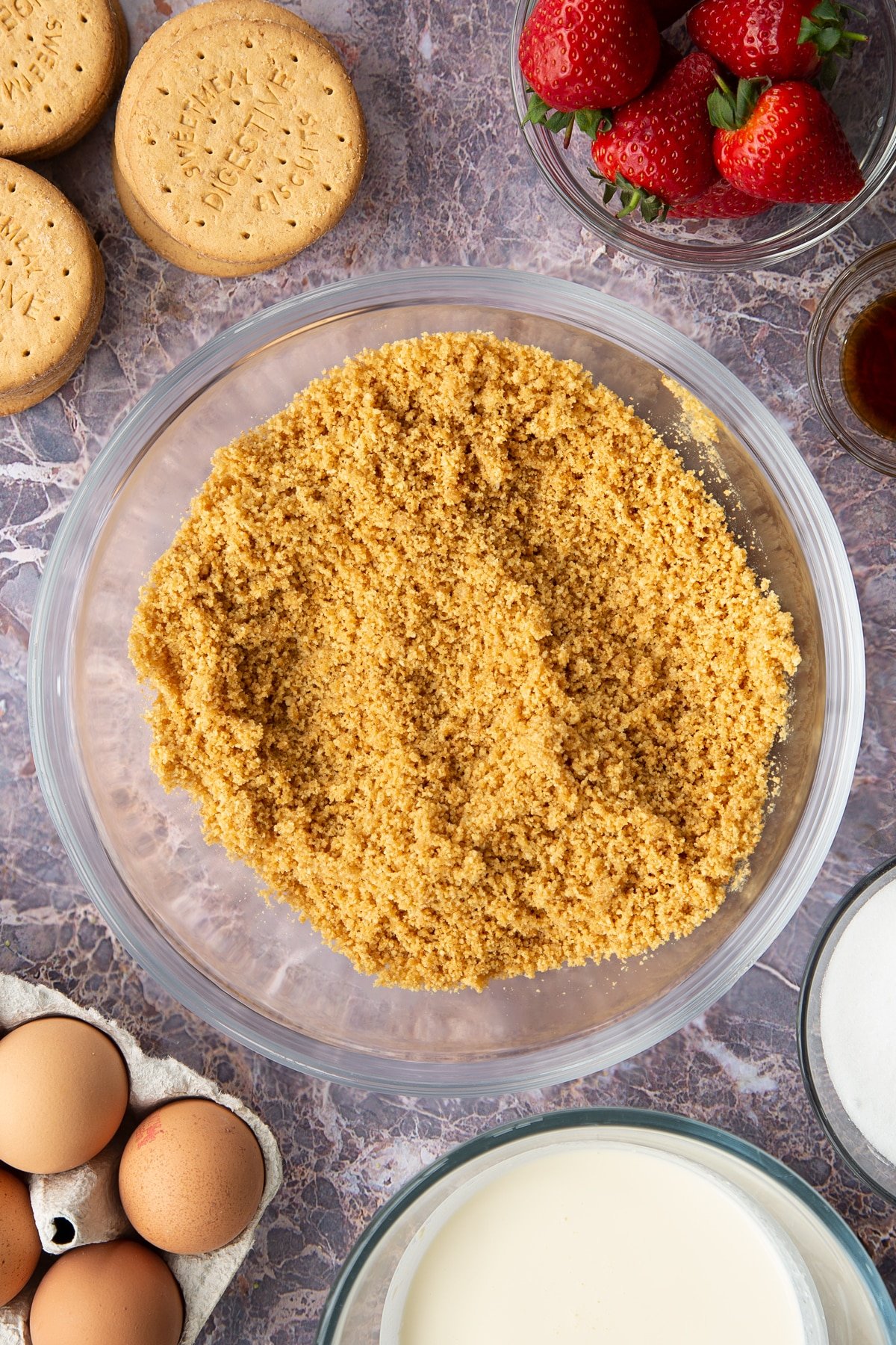 buttery digestive crumbs in a large clear bowl surrounded by strawberries and digestive biscuits.