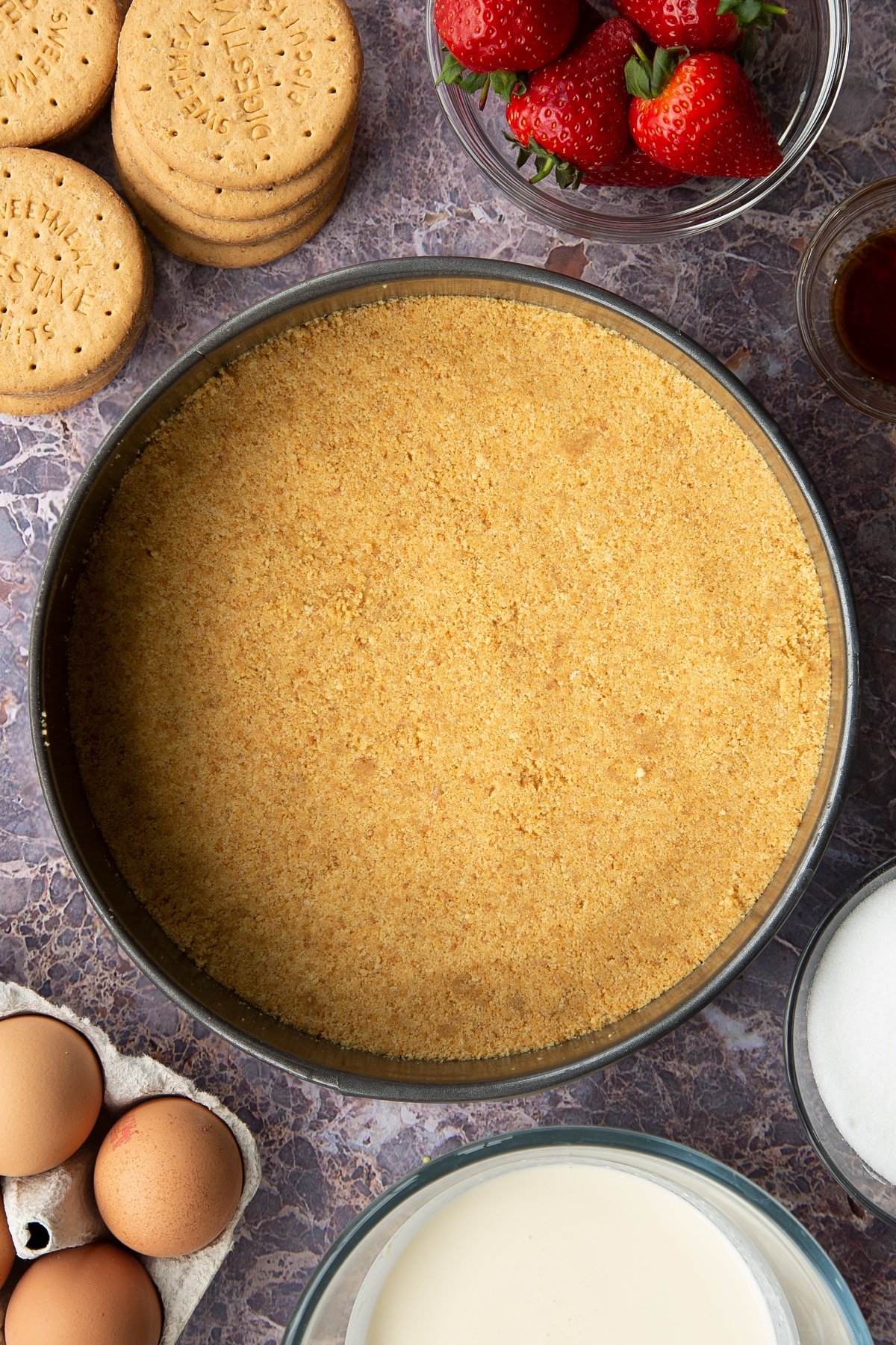 buttery digestive crumbs in a large springform cake tin pressedd down to create a solid base surrounded by strawberries and digestive biscuits.