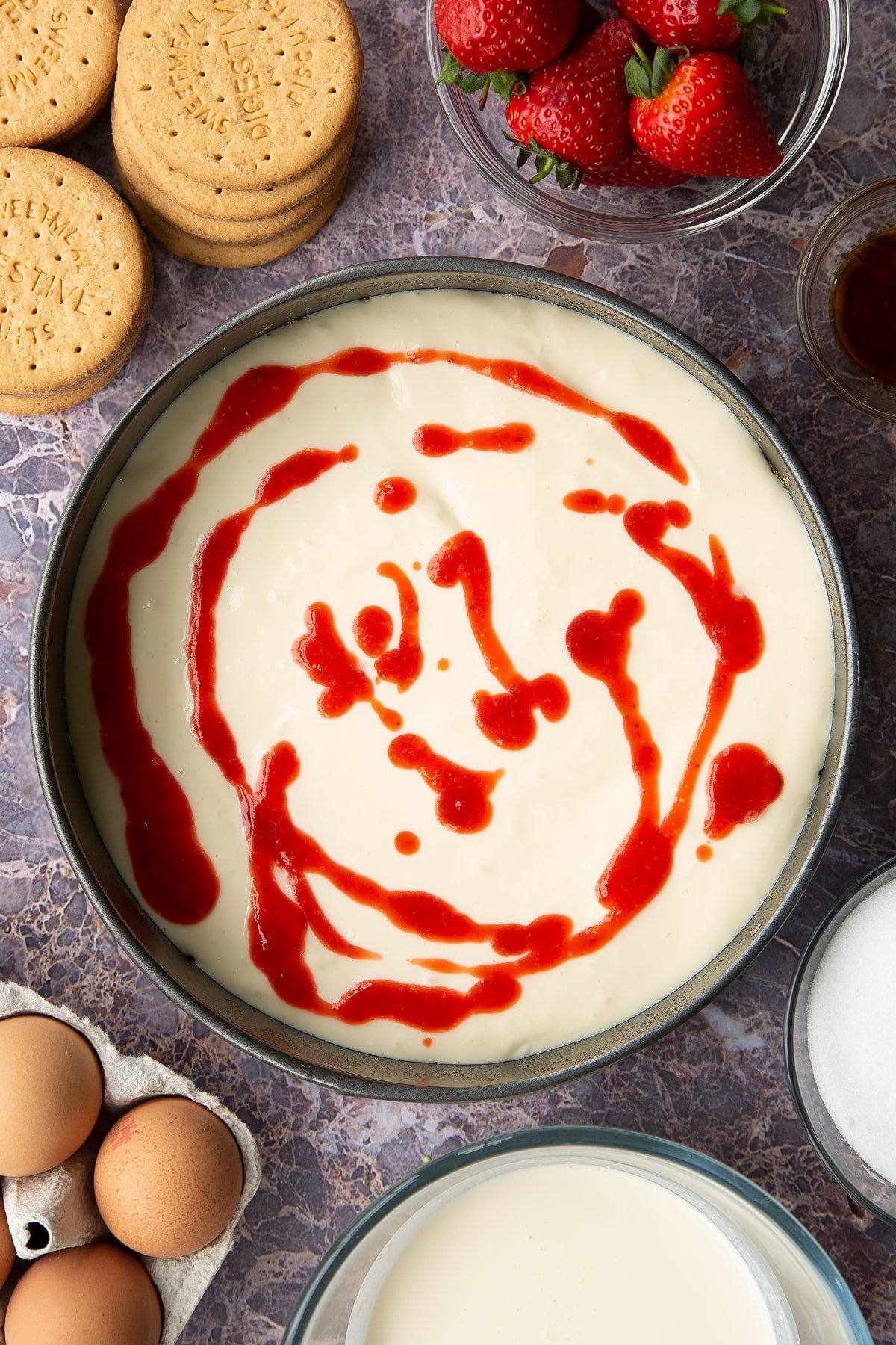 cheesecake batter in a springform cake tin topped with strawberry sauce.