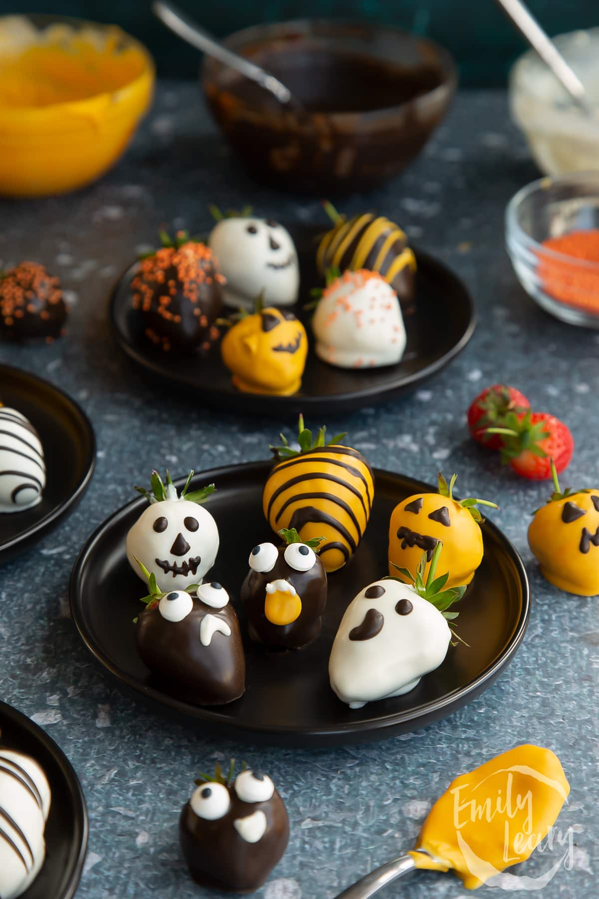 Wide shot of the finished halloween chocolate covered strawberries served on a black plate.