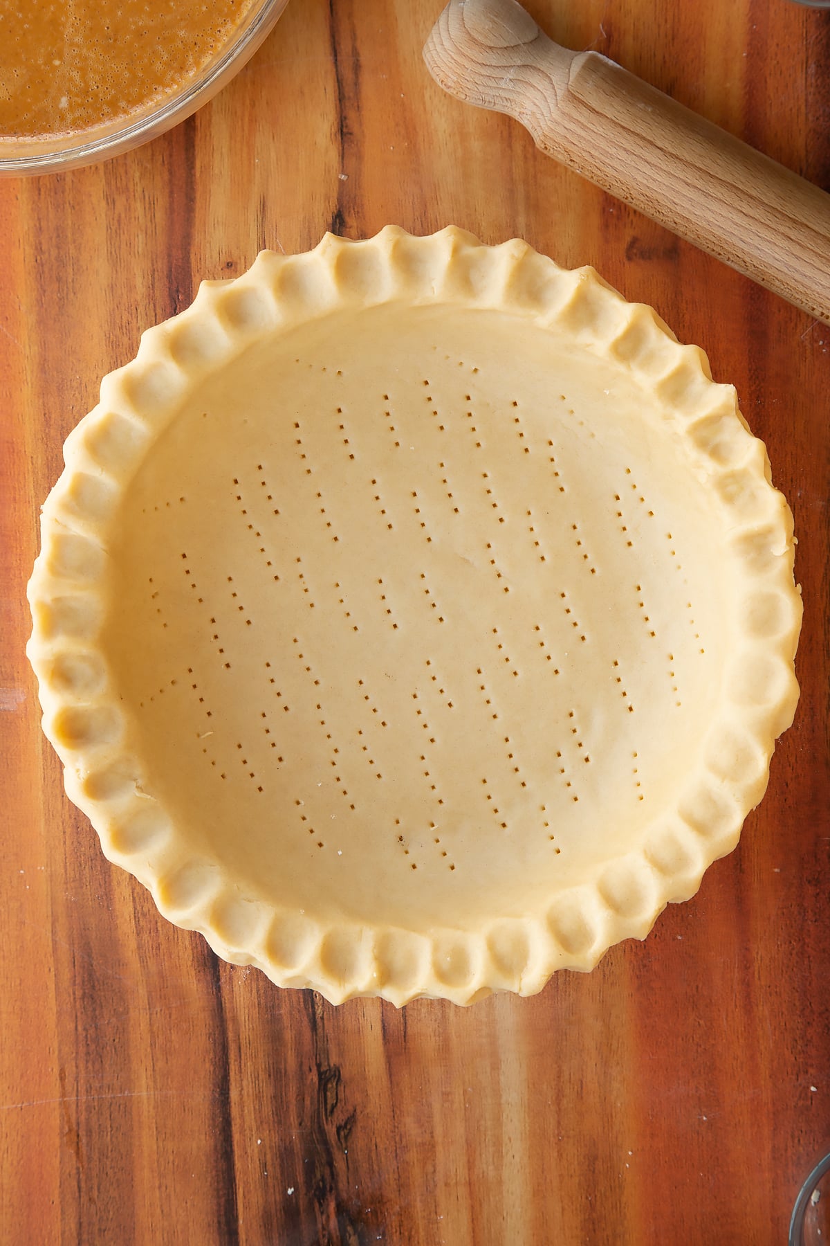 Adding fork holes to the base of the caramel pumpkin pie inside the pie dish.