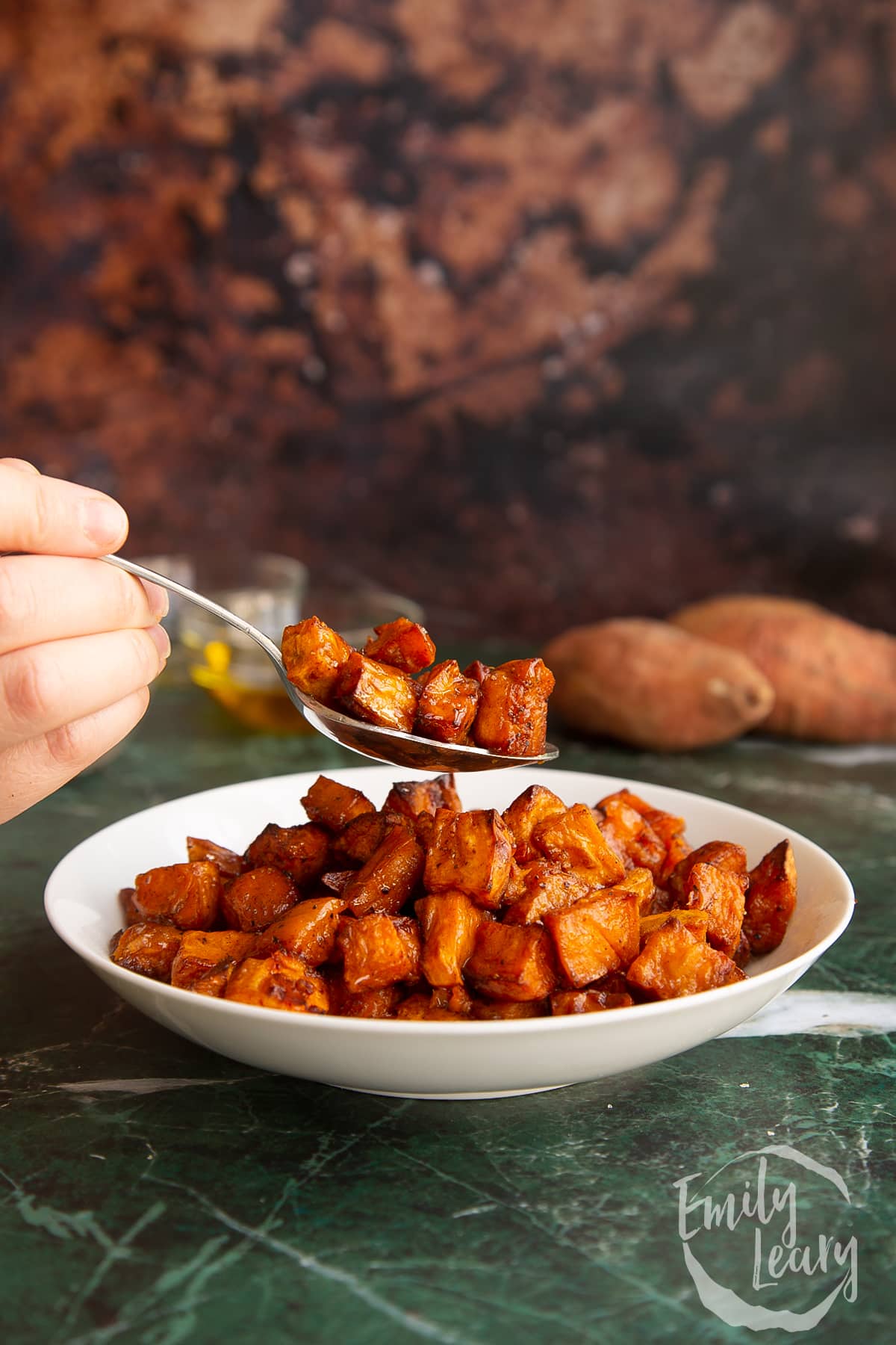 A spoon over a bowl filled with caramelised sweet potatoes.