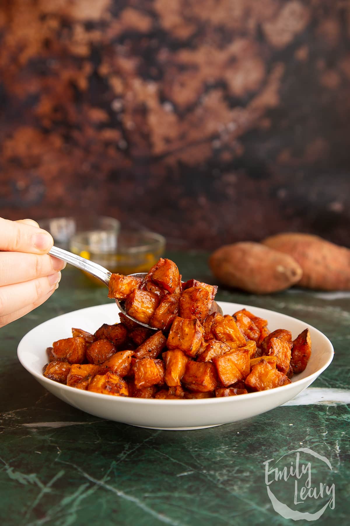 Spoon going into a bowl of finished caramelised sweet potatoes.