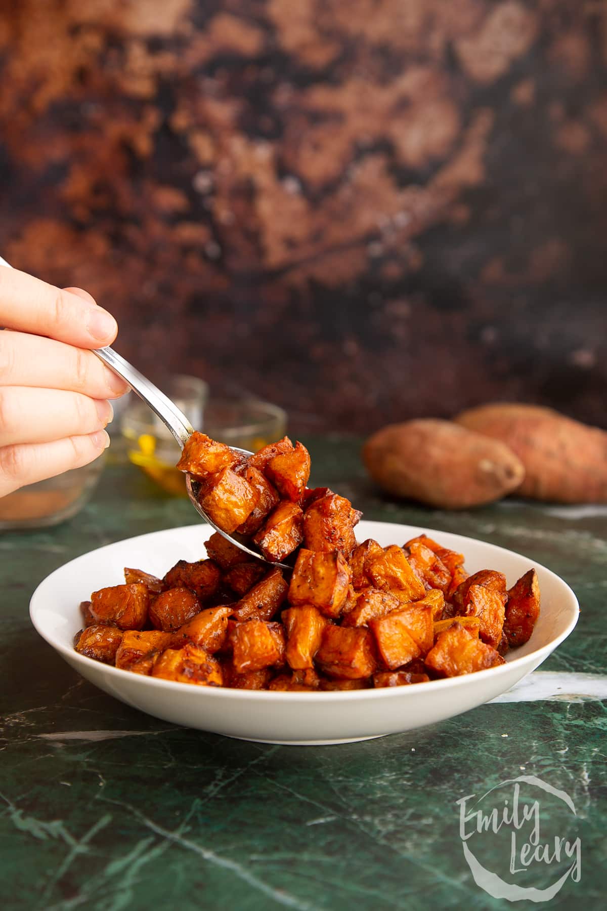 A spoon going into a bowl of finished caramelised sweet potatoes.